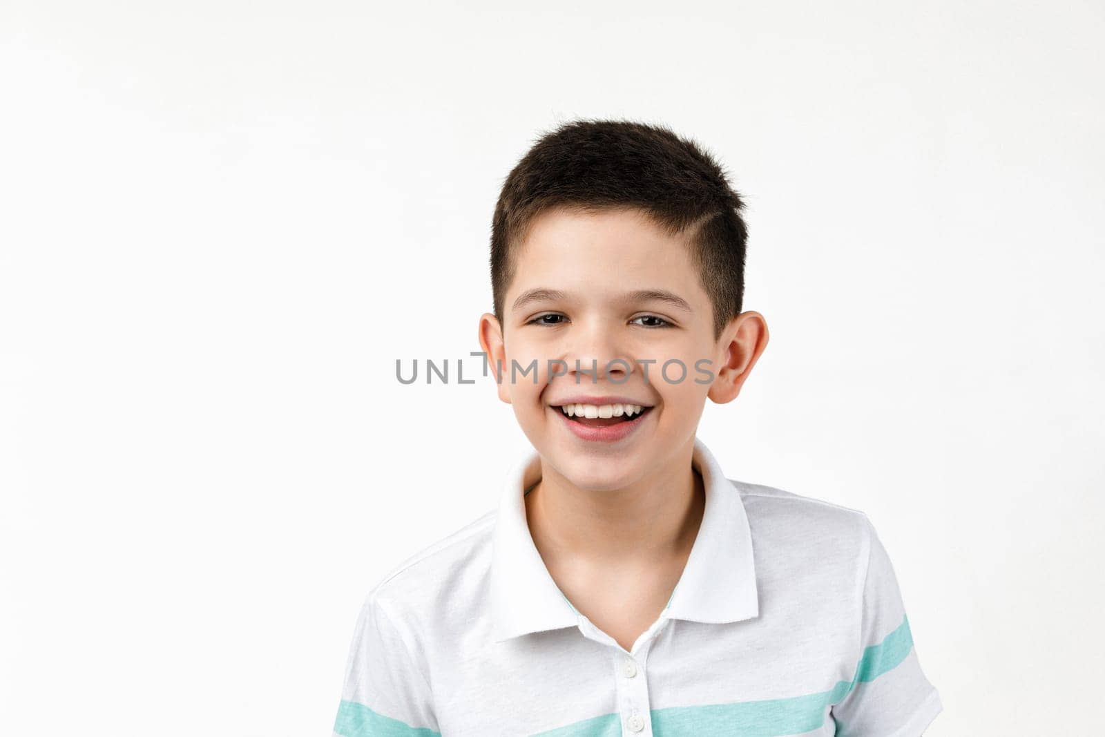 Cute smiling little child boy in t-shirt looking at the camera on white background. Human emotions and facial expression