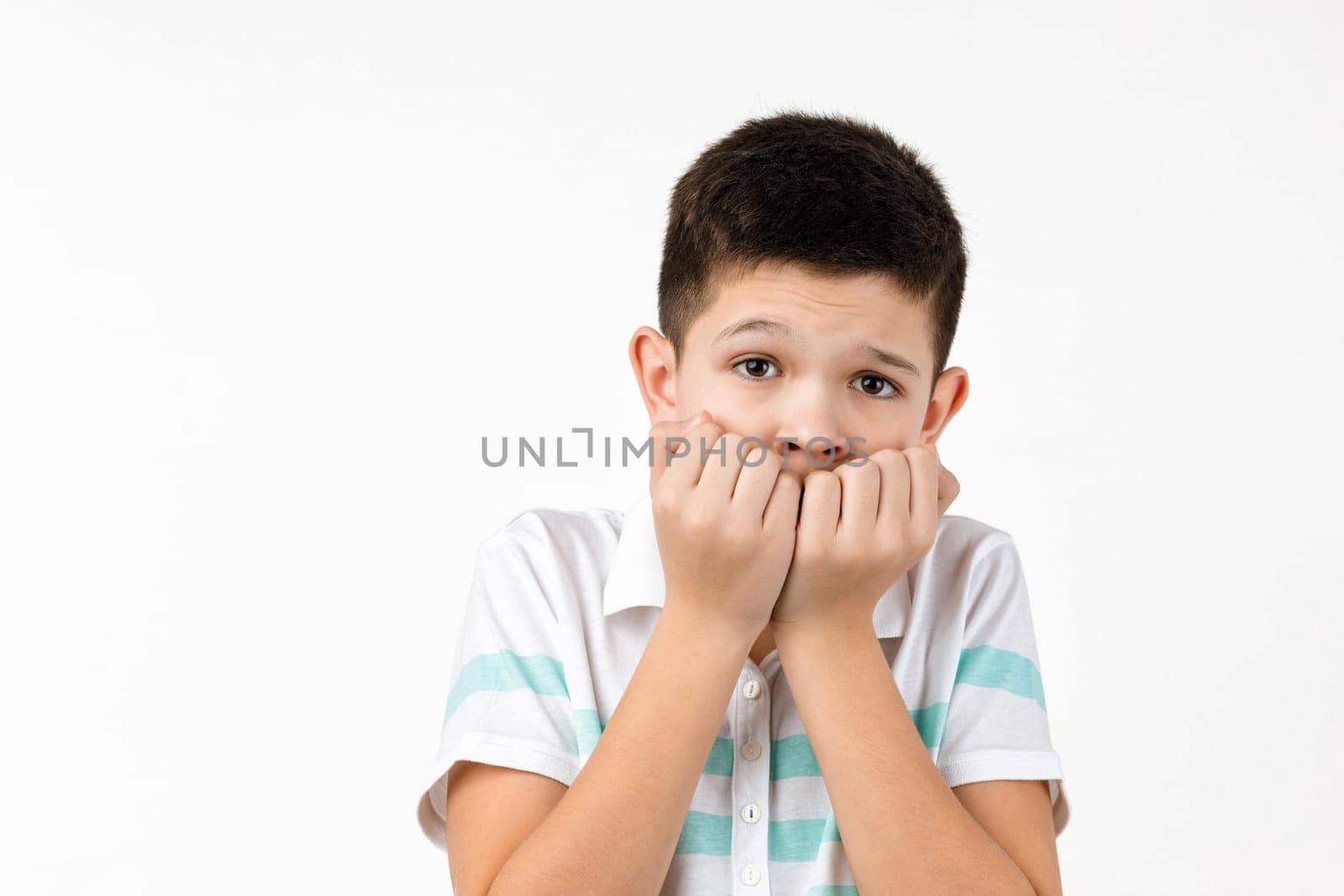 Cute scared little child boy in t-shirt looking at the camera on white background. Human emotions and facial expression