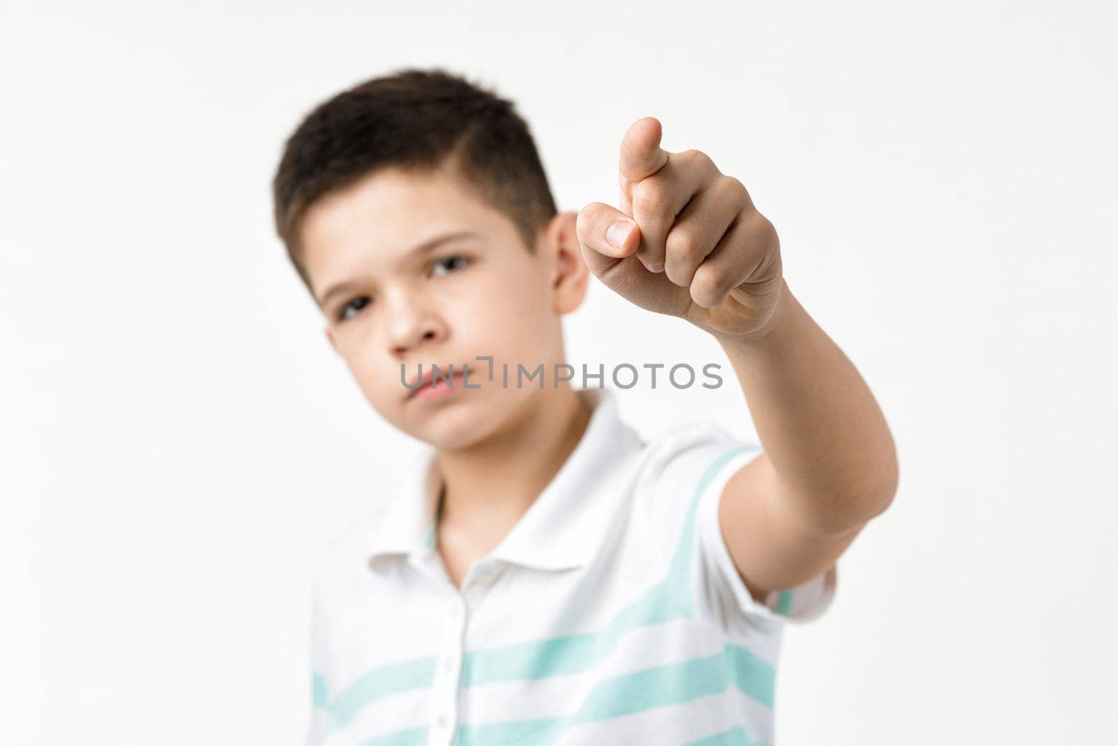 Cute little boy in striped t-shirt pointing camera on white background. child pointing at you. focus on hand