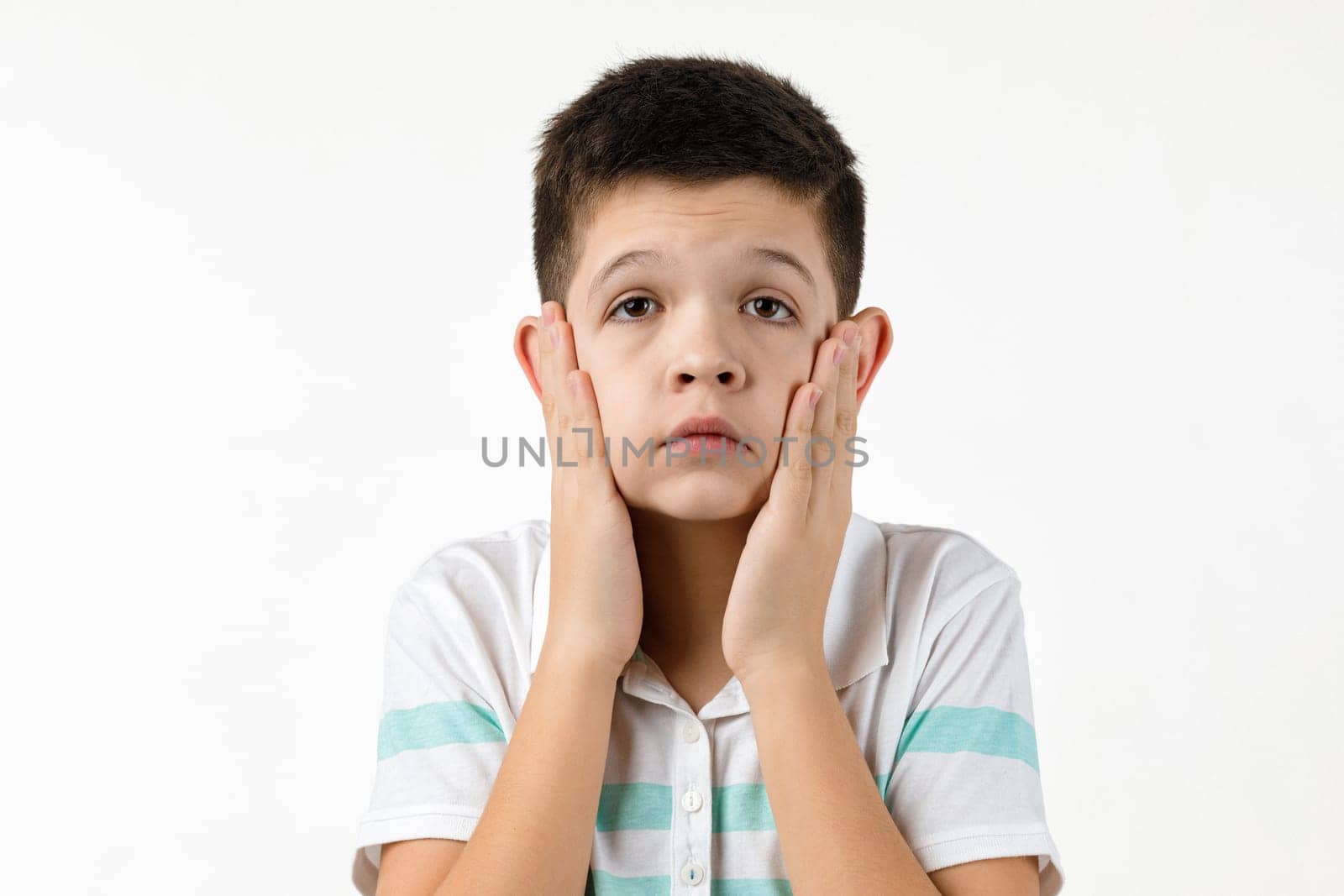 offended sad little child boy in striped t-shirt on white background. Human emotions and facial expression