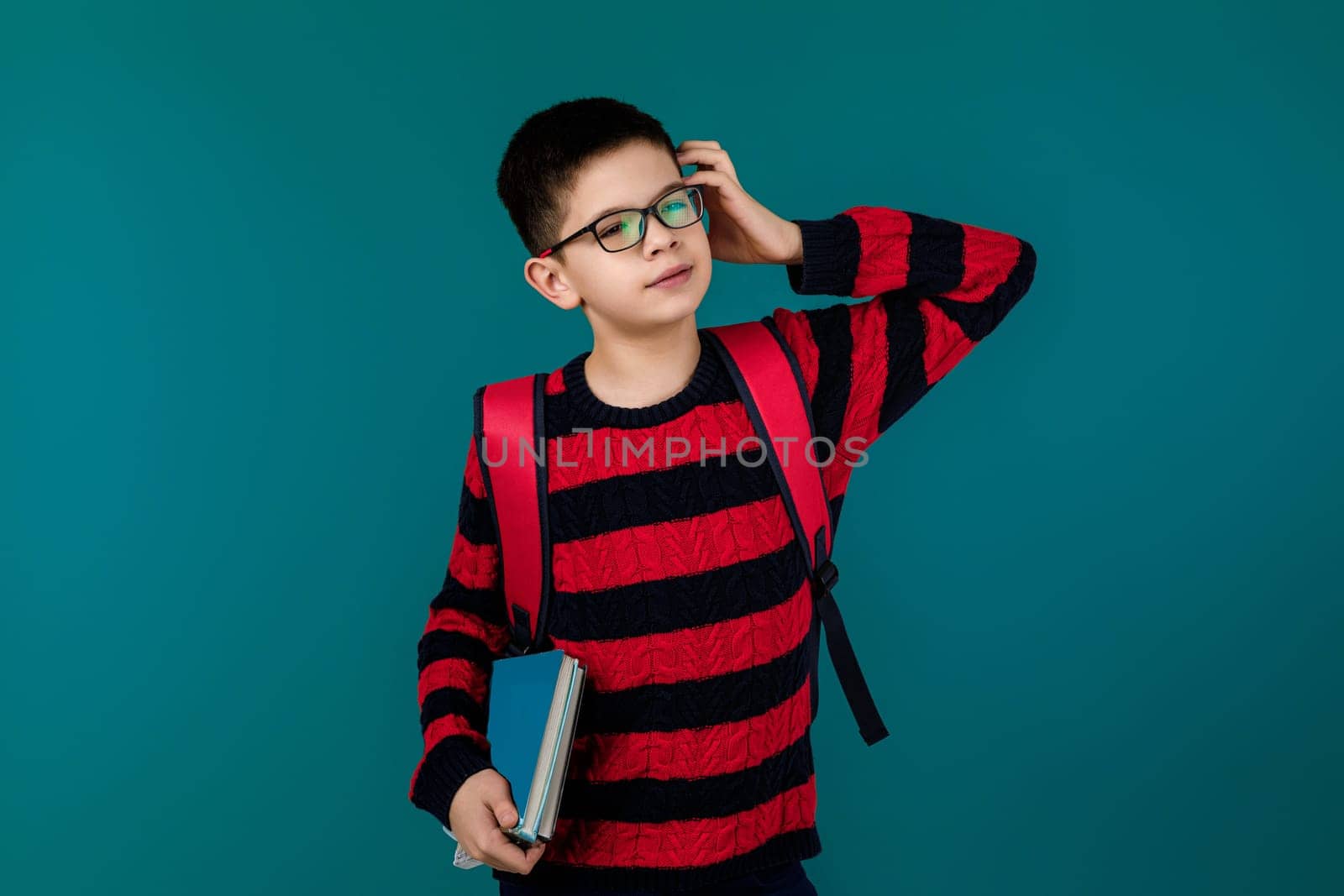 little cheerful school boy wearing glasses holding a book over blue background