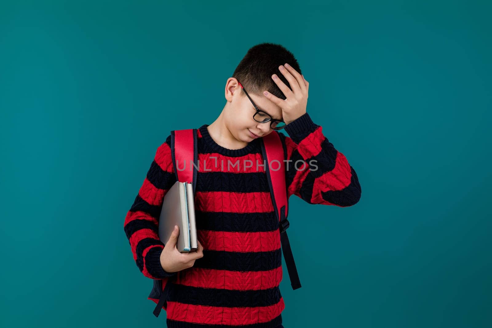 little cheerful school boy wearing glasses holding a book over blue background. the child is tired of studying and homework