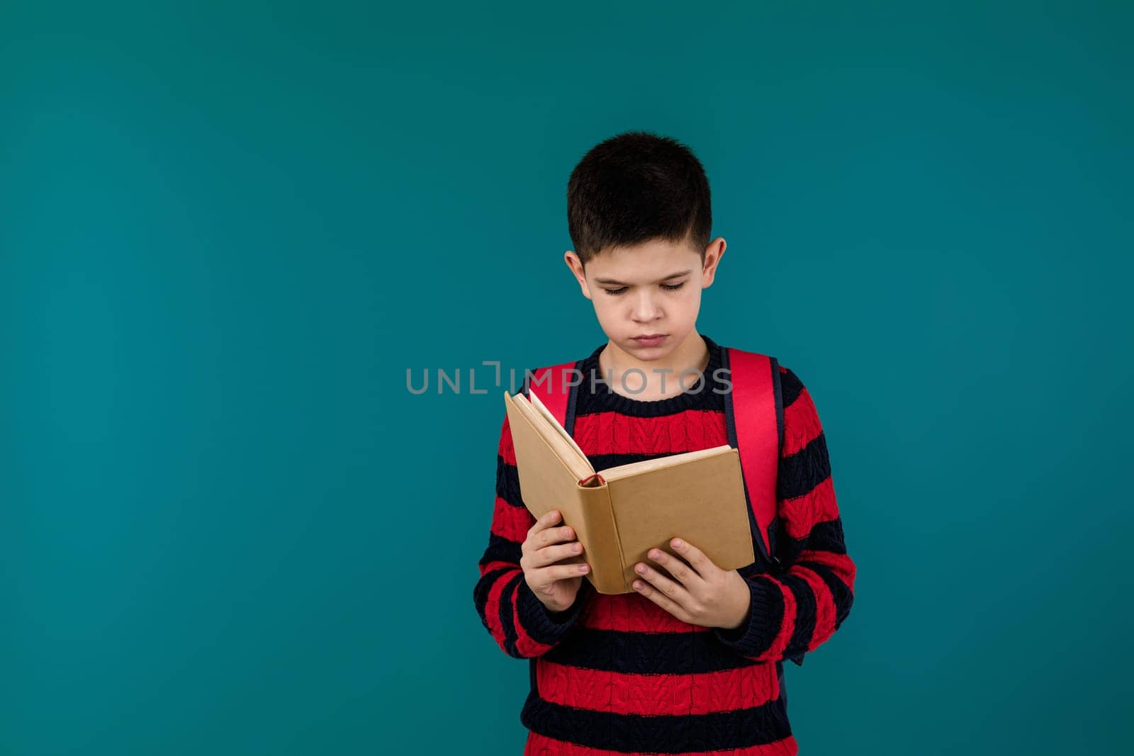 little cheerful school boy reading book over blue background, copy space. School concept.