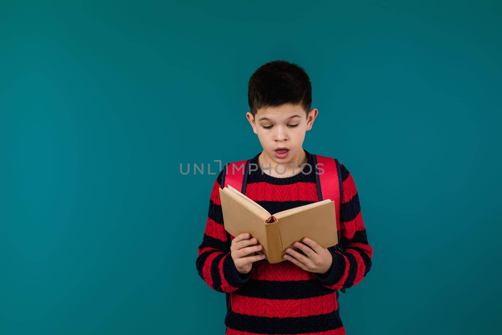 little cheerful school boy reading interesting book over blue background, copy space. School concept.