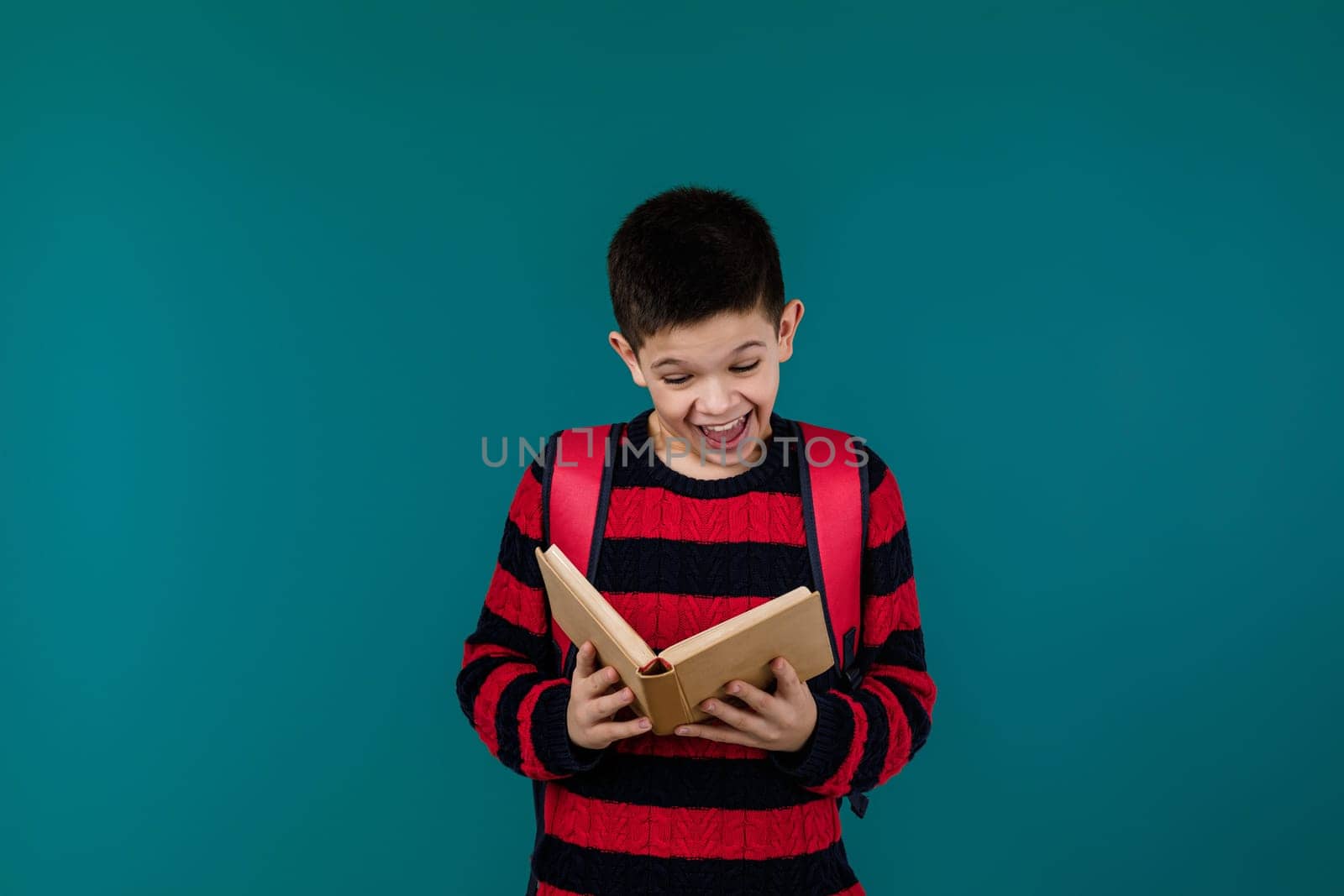 smiling little cheerful school boy reading interesting book over blue background, copy space. School concept.
