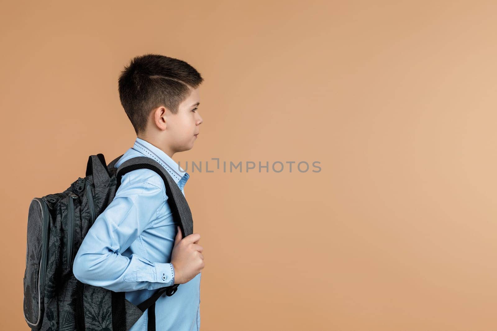 little cute school boy with gray backpack over yellow background. copy space