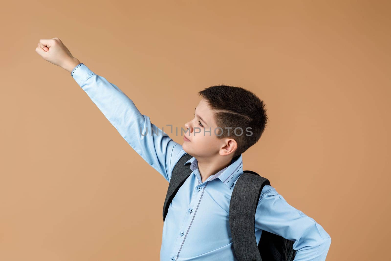 little cute school boy with backpack in superhero pose over yellow background. child ready to save the world. kid clenches his fist