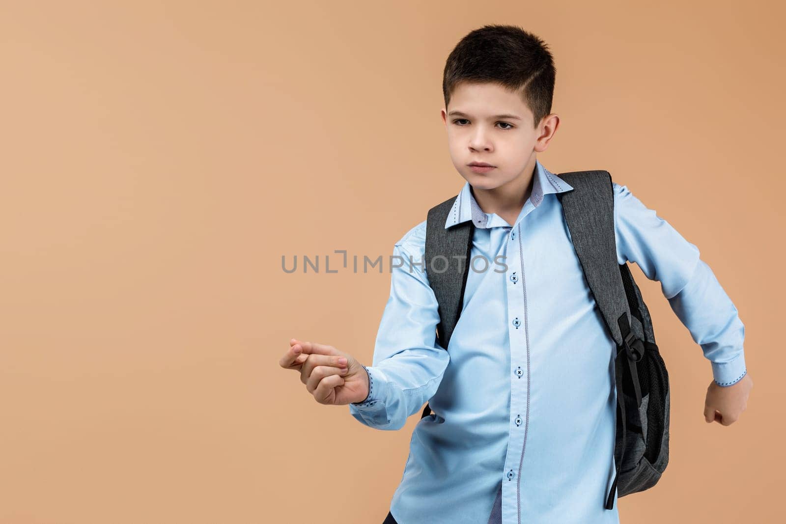 little cute school boy with gray backpack dancing over soft yellow background. copy space. happy back to school