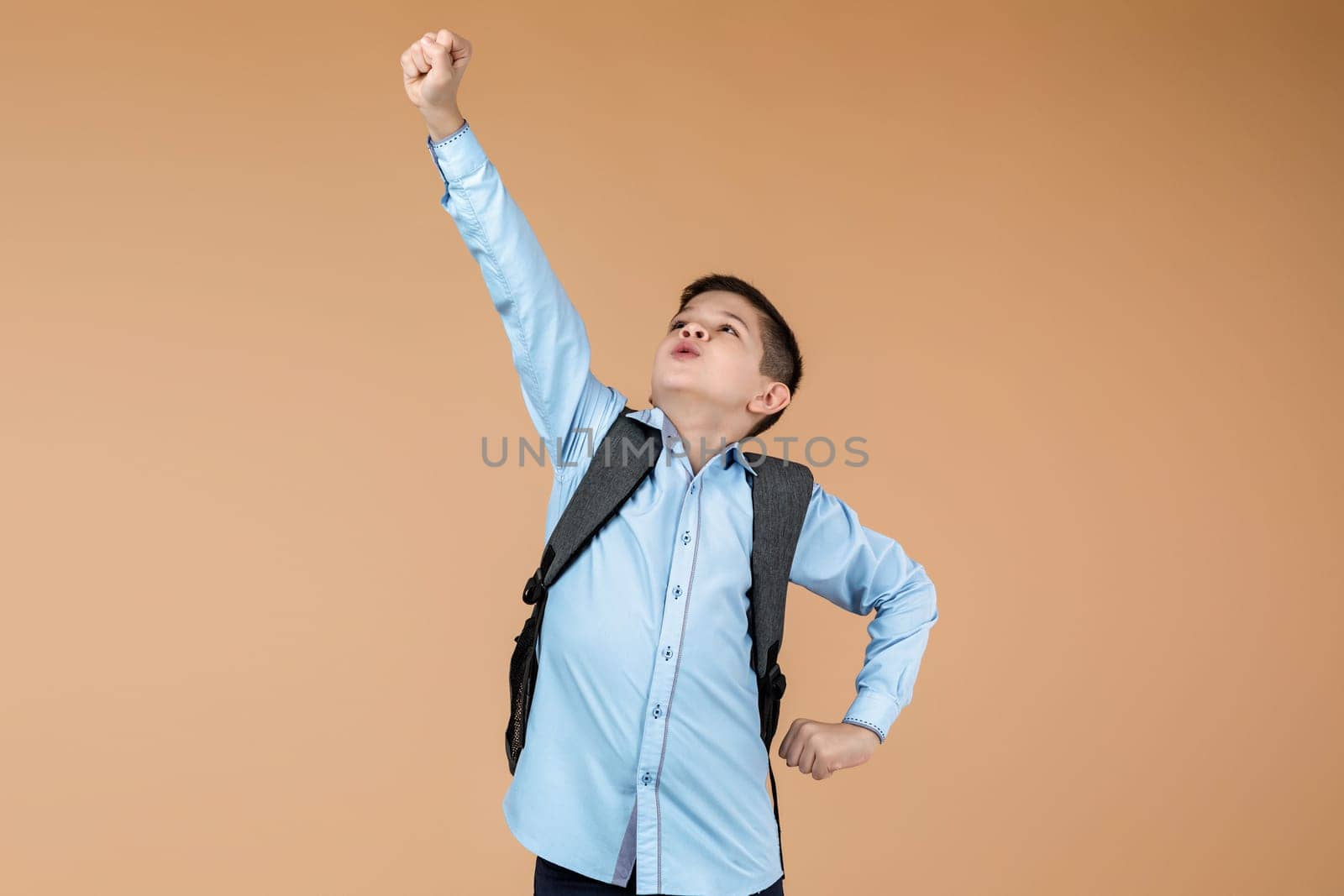 little cute school boy with backpack in superhero pose over yellow background. child ready to save the world. kid clenches his fist