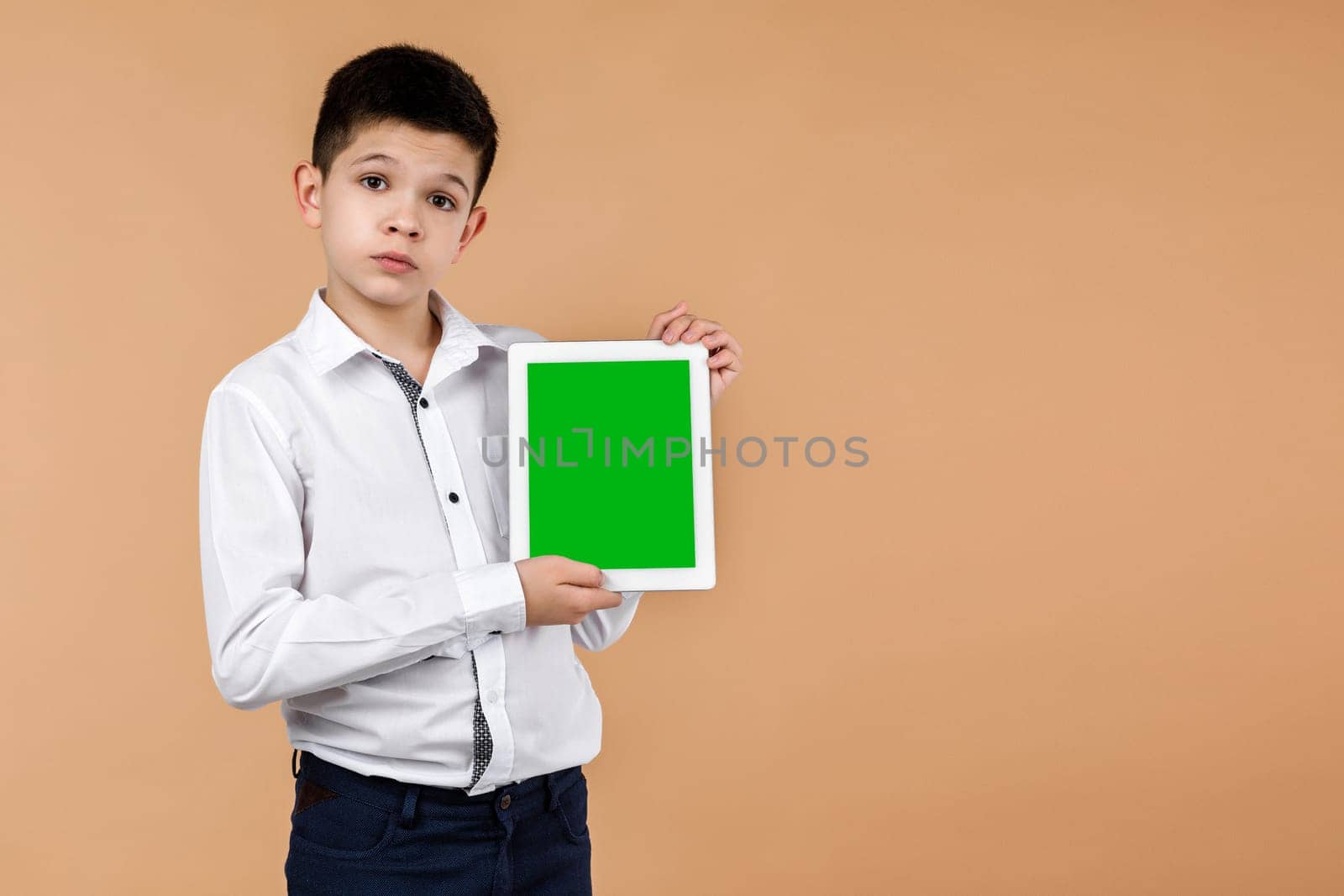 Little boy with tablet on light yellow studio background. he showing something on screen. space for text. moke up