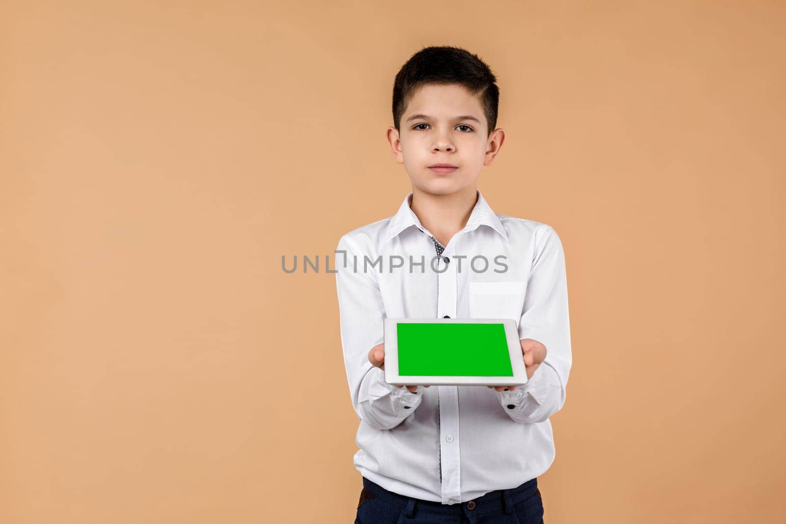 Little boy with tablet on light yellow studio background. he showing something on screen. space for text. moke up
