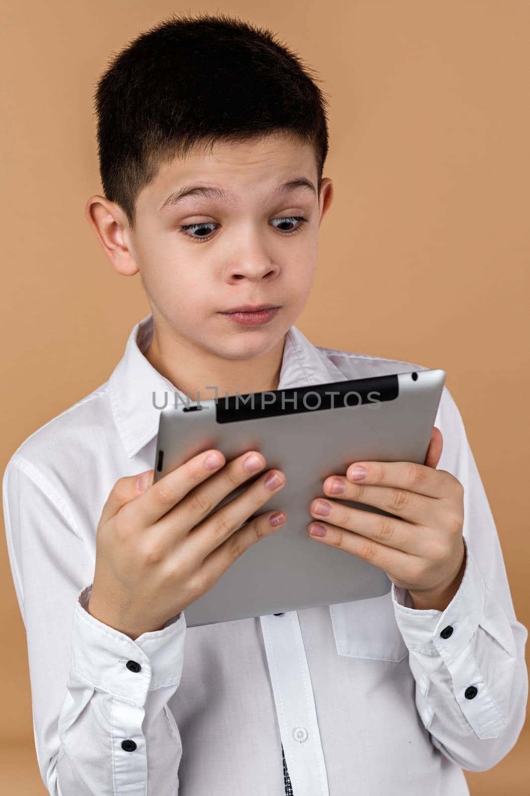Little surprised boy using tablet on light yellow studio background.