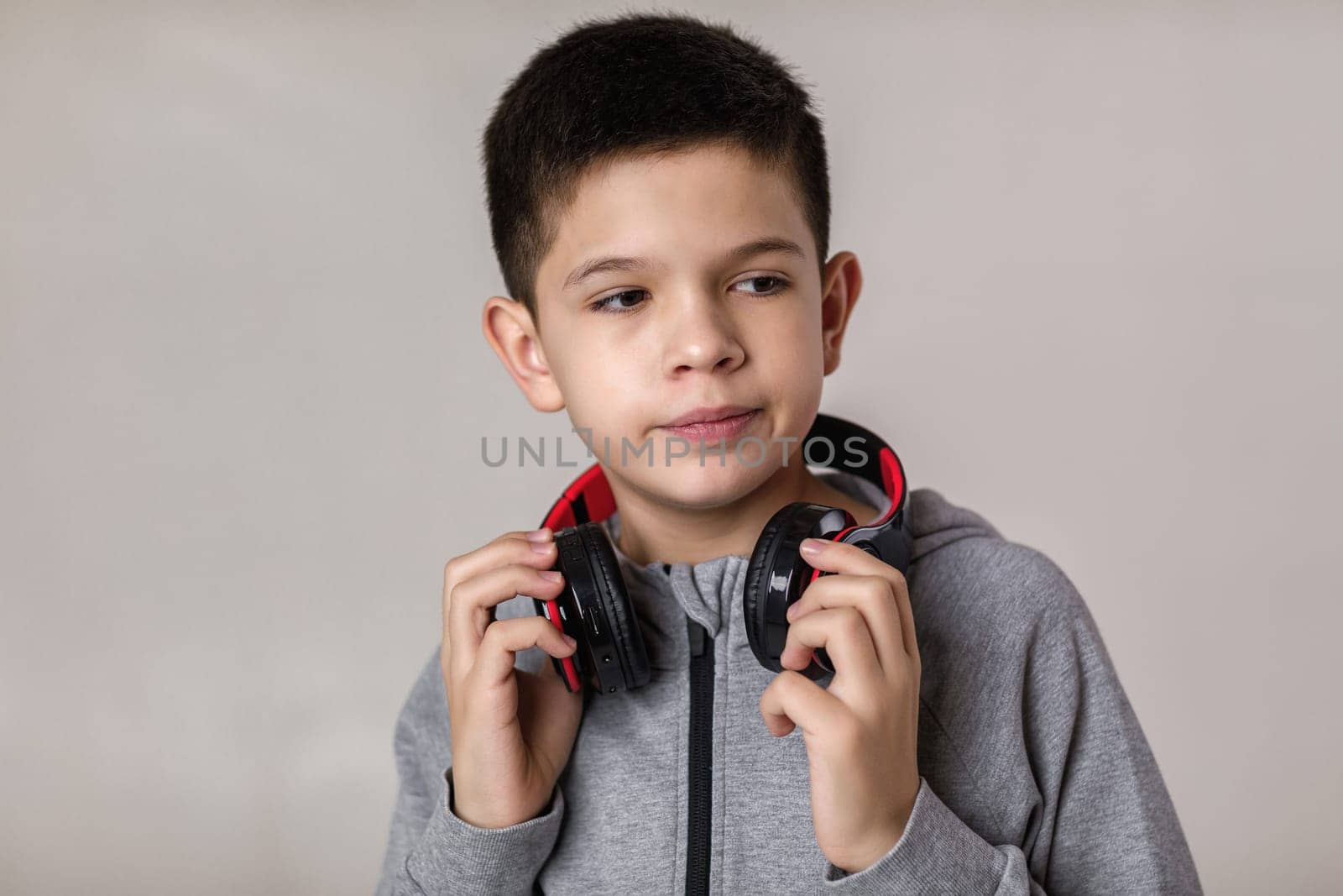 Happy child boy with headphones looking at camera over gray background.