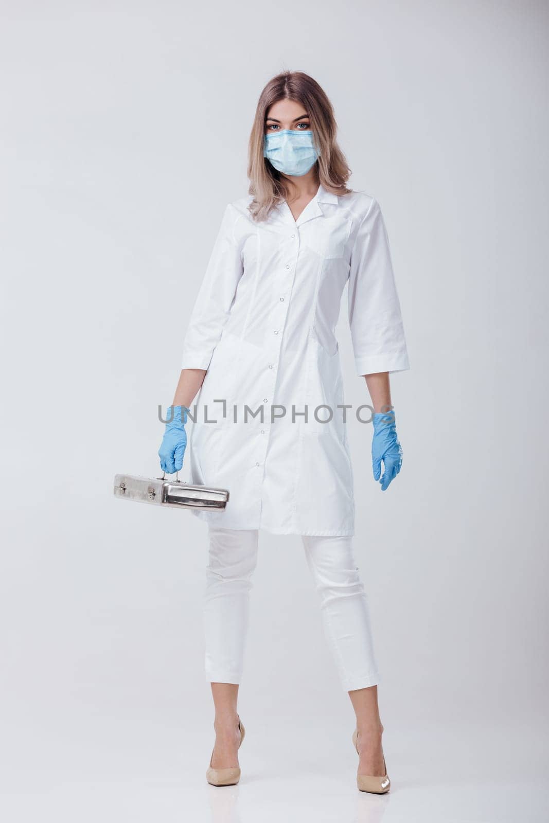 woman doctor with face mask and medical gloves holds a metal bag with medical instruments