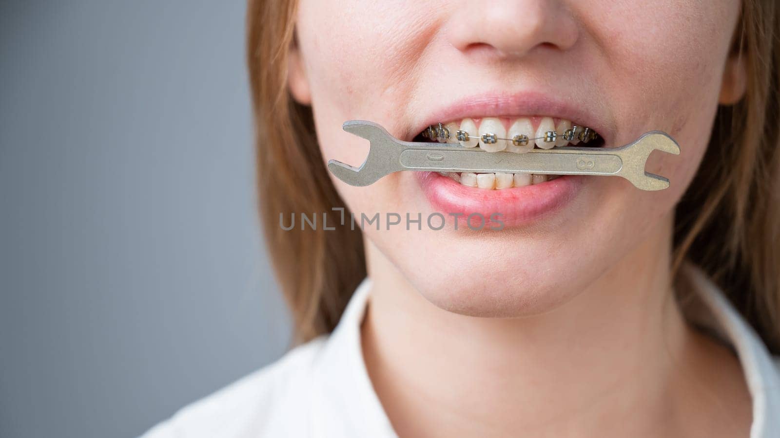 Close-up portrait of a woman with braces holding a wrench in her teeth