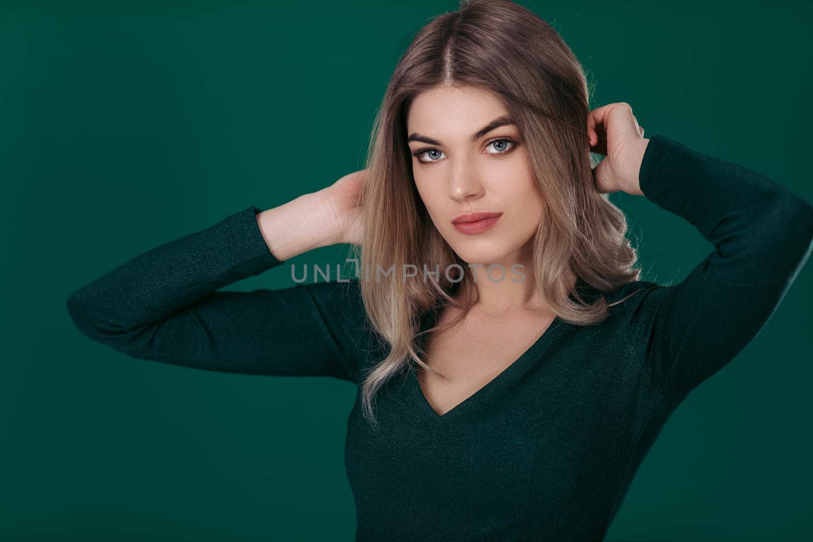 Sensual beautiful blonde woman looking at camera and posing in green dress on green background