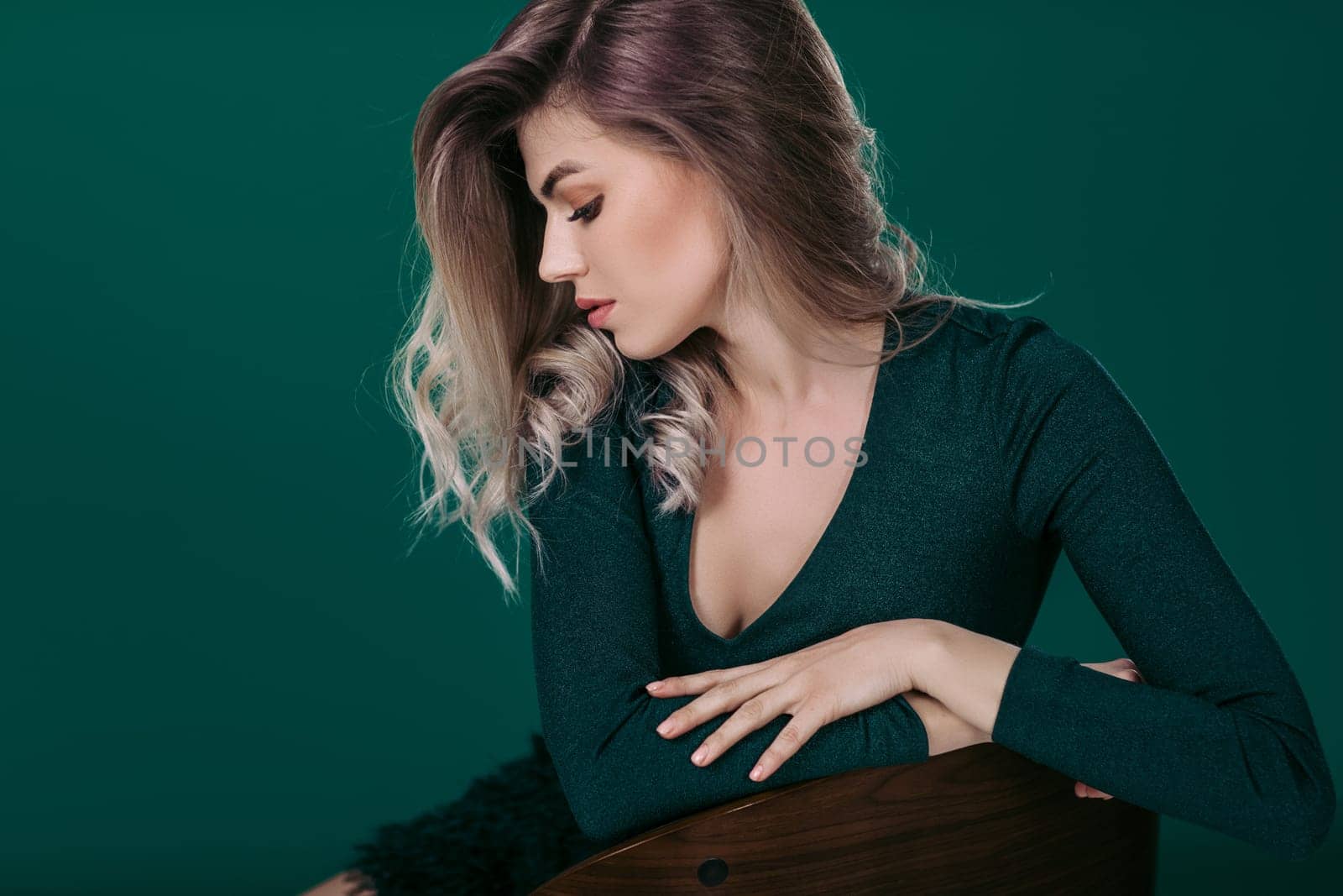 fashion portrait of sensual beautiful blonde woman in green dress sitting on chair against green background