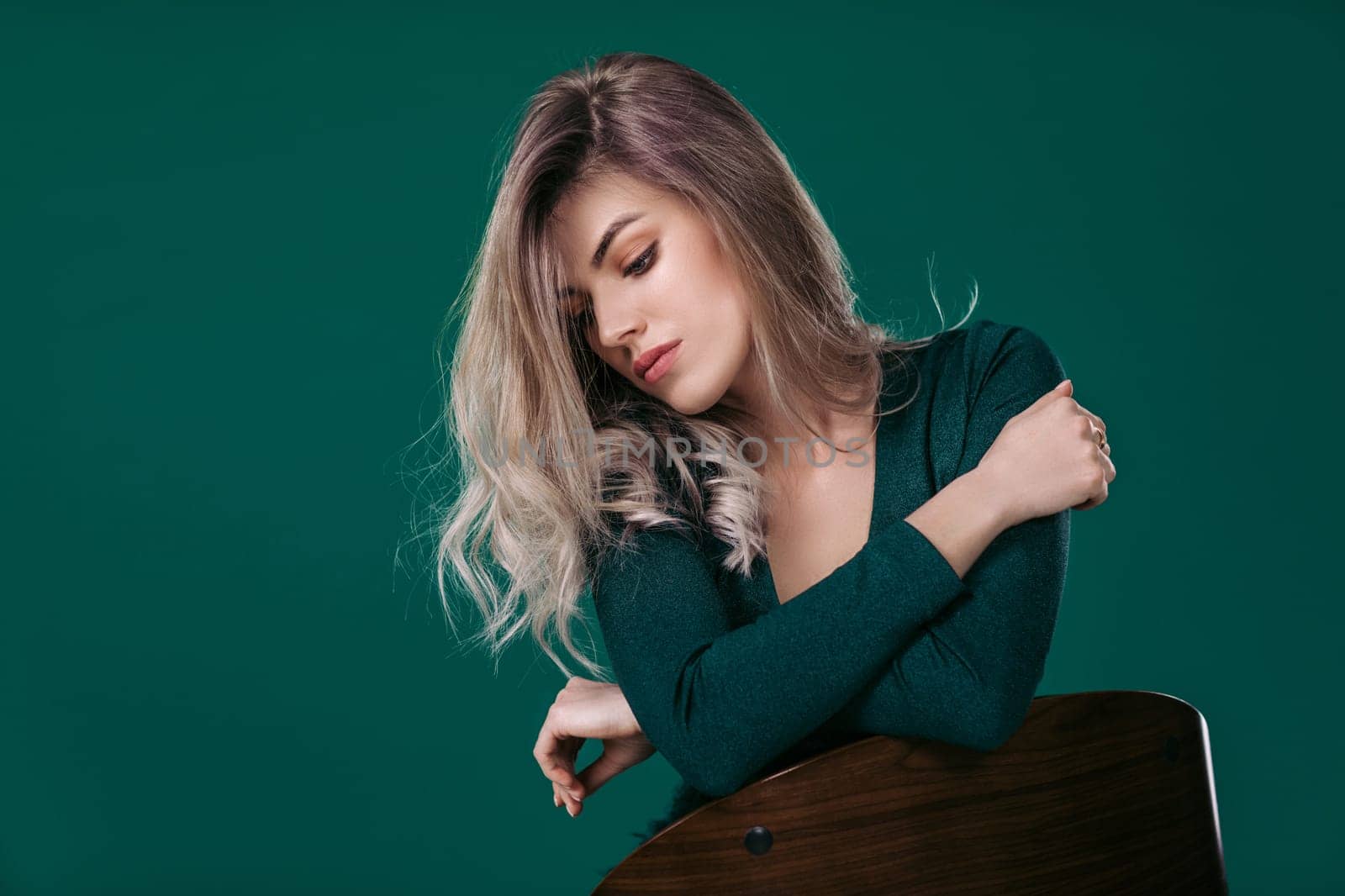 Sensual beautiful blonde woman in green dress sitting on chair against green background