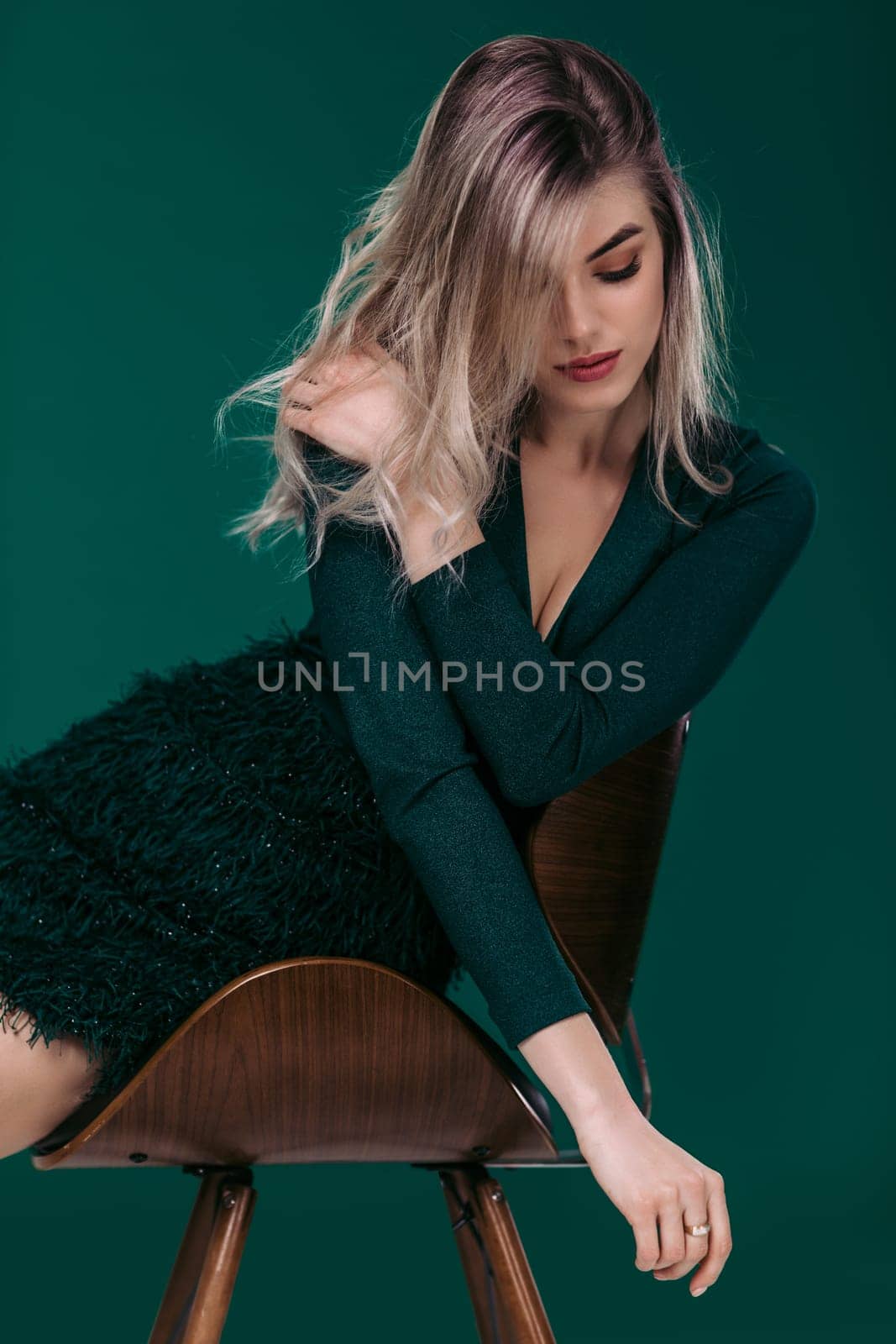 fashion portrait of sexy sensual beautiful blonde woman in green dress sitting on chair against green background