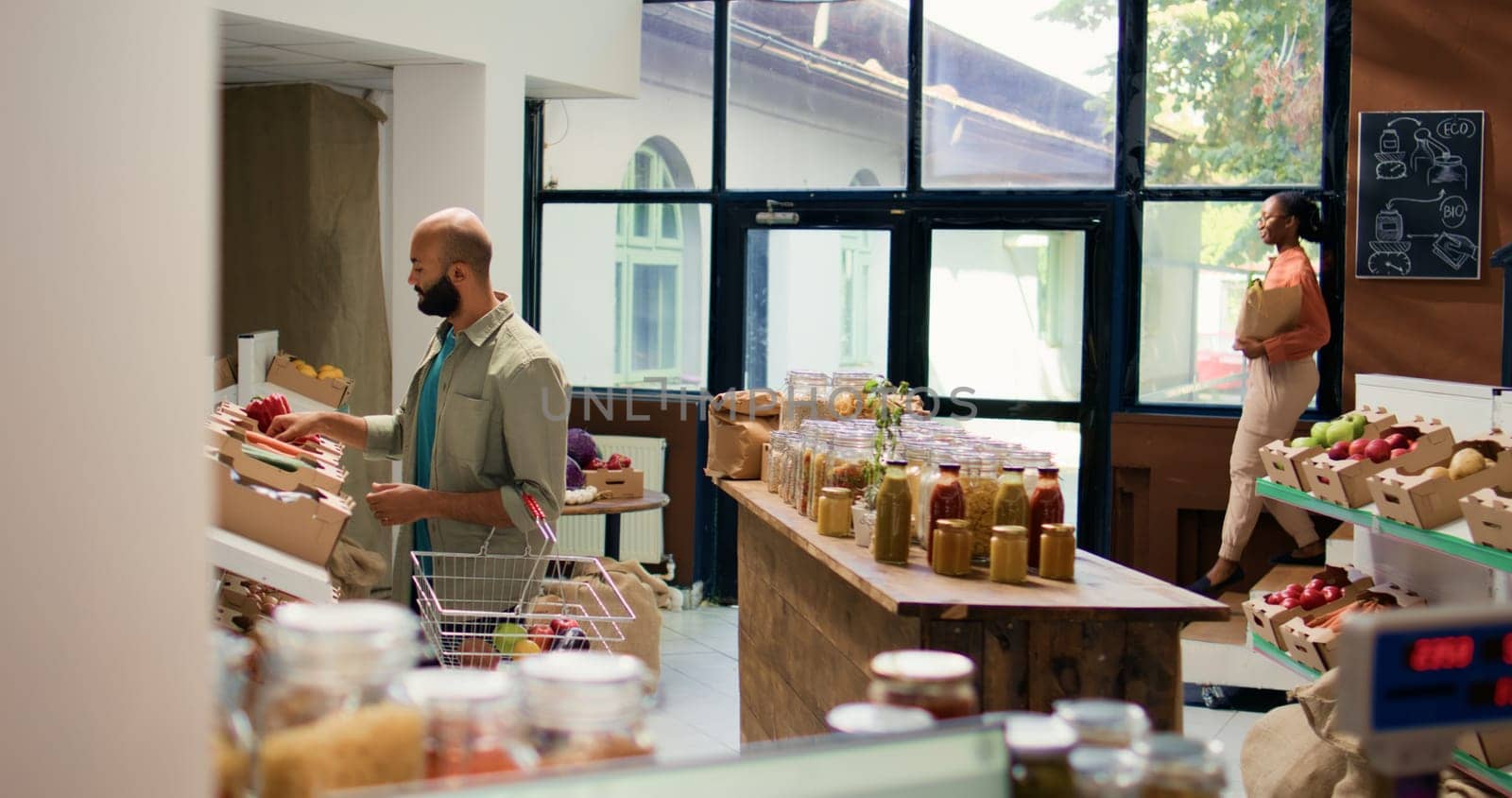 Customer looking at fresh veggies on shelves at local zero waste eco store, choosing to buy homegrown produce for sustainable lifestyle and vegan nutrition. Man doing shopping at ecological shop.