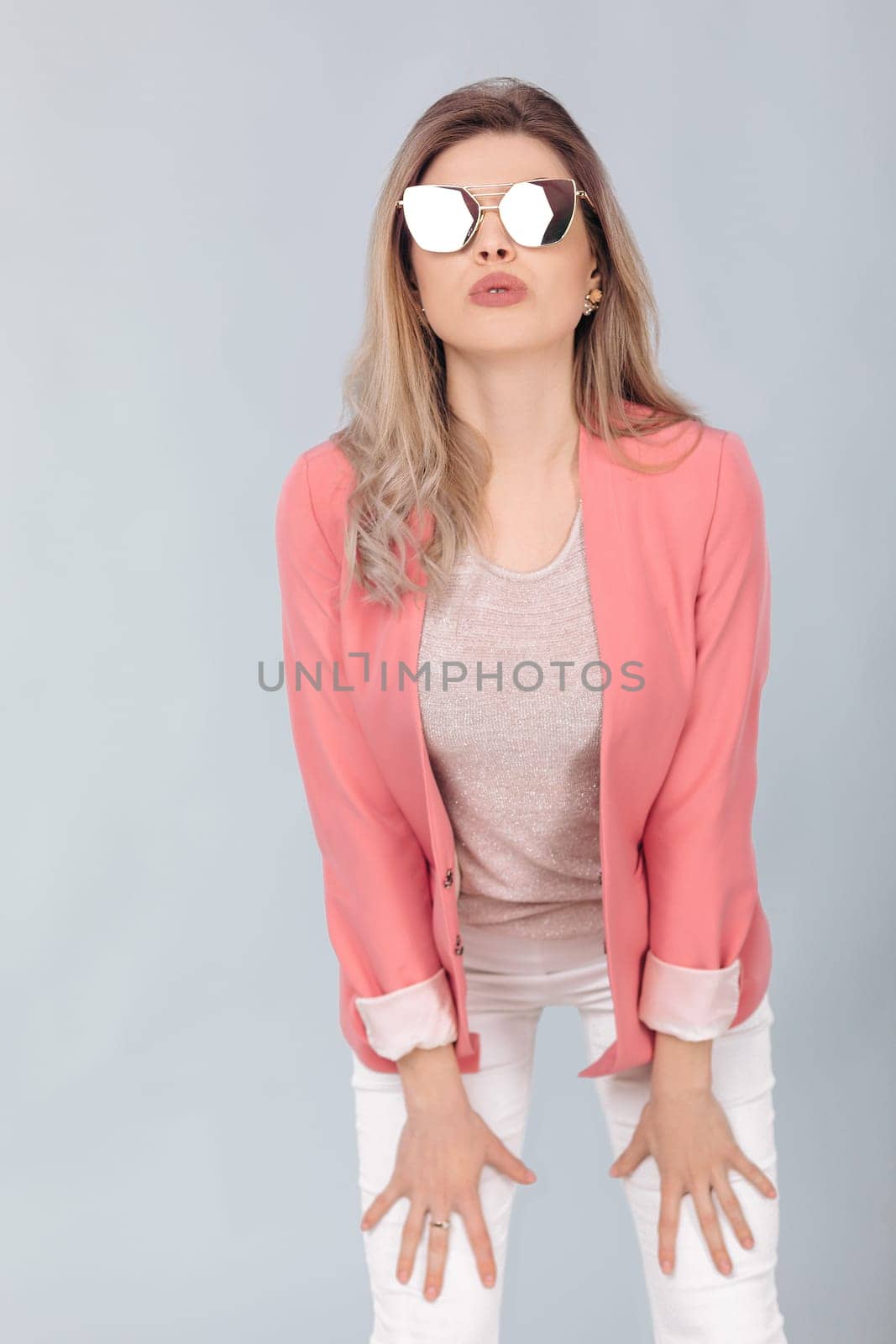 Fashion portrait of attractive elegant blonde woman in pastel pink jacket and sunglasses posing in studio. woman dressed in trendy spring outfit