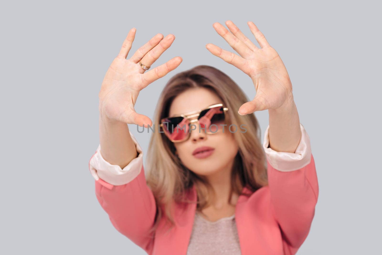 Fashion portrait of attractive woman in pastel pink jacket showing stop gesture