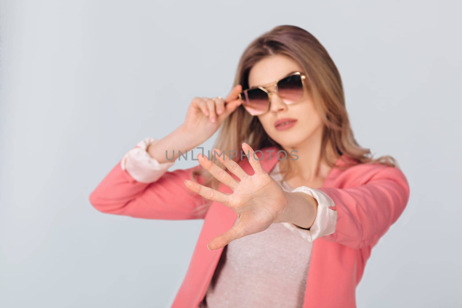 Fashion portrait of attractive woman in pastel pink jacket showing stop gesture