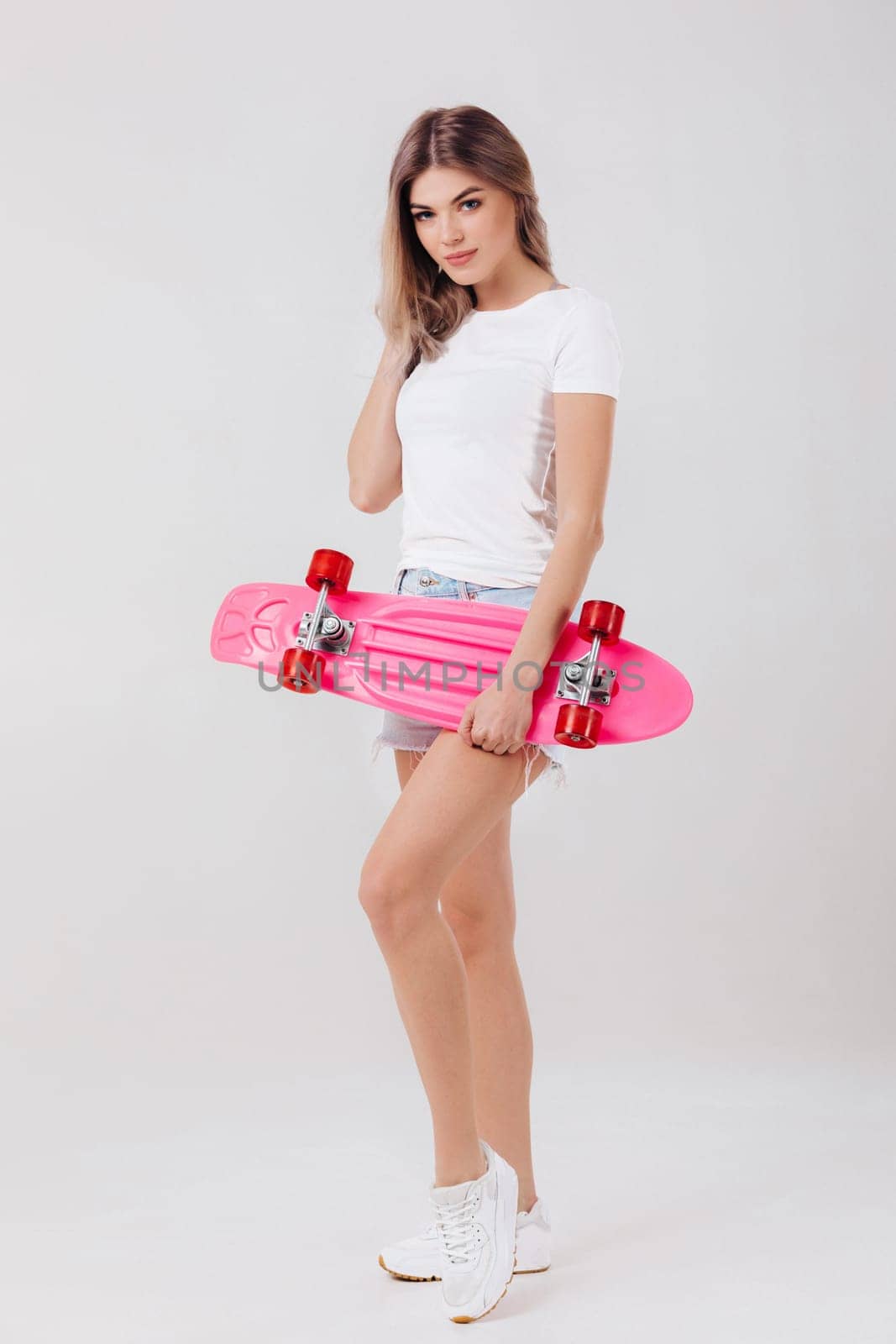 attractive woman blonde in white t-shirt and denim shorts holding pink skateboard