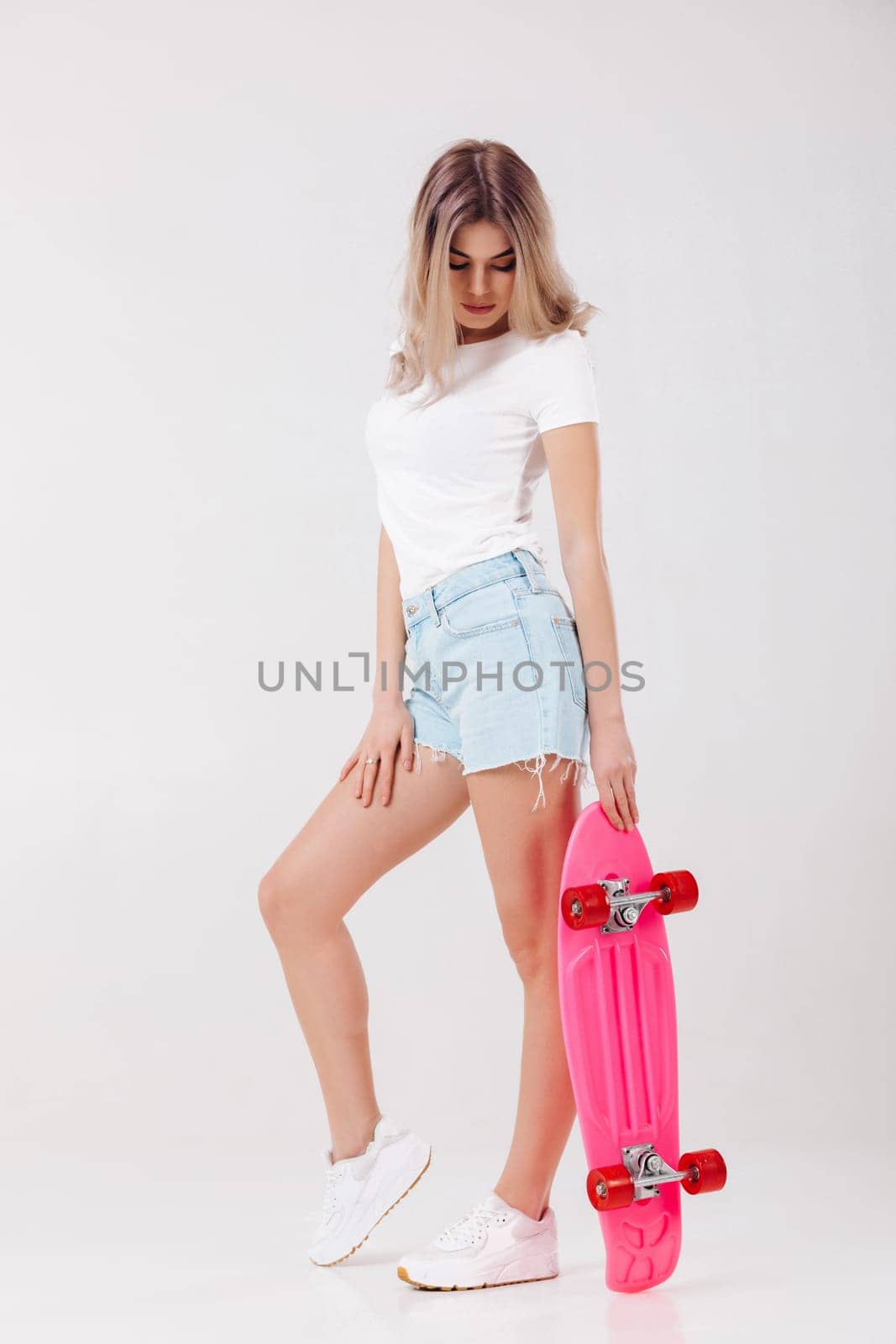 beautiful woman in white t-shirt and denim shorts with pink skateboard