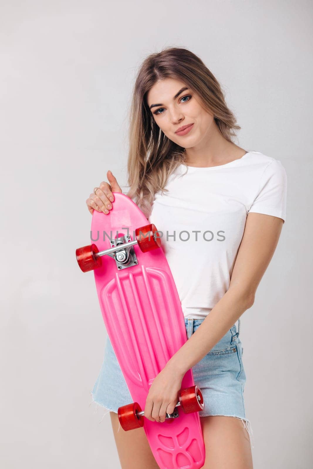 attractive smiling woman blonde in white t-shirt and denim shorts holding pink skateboard