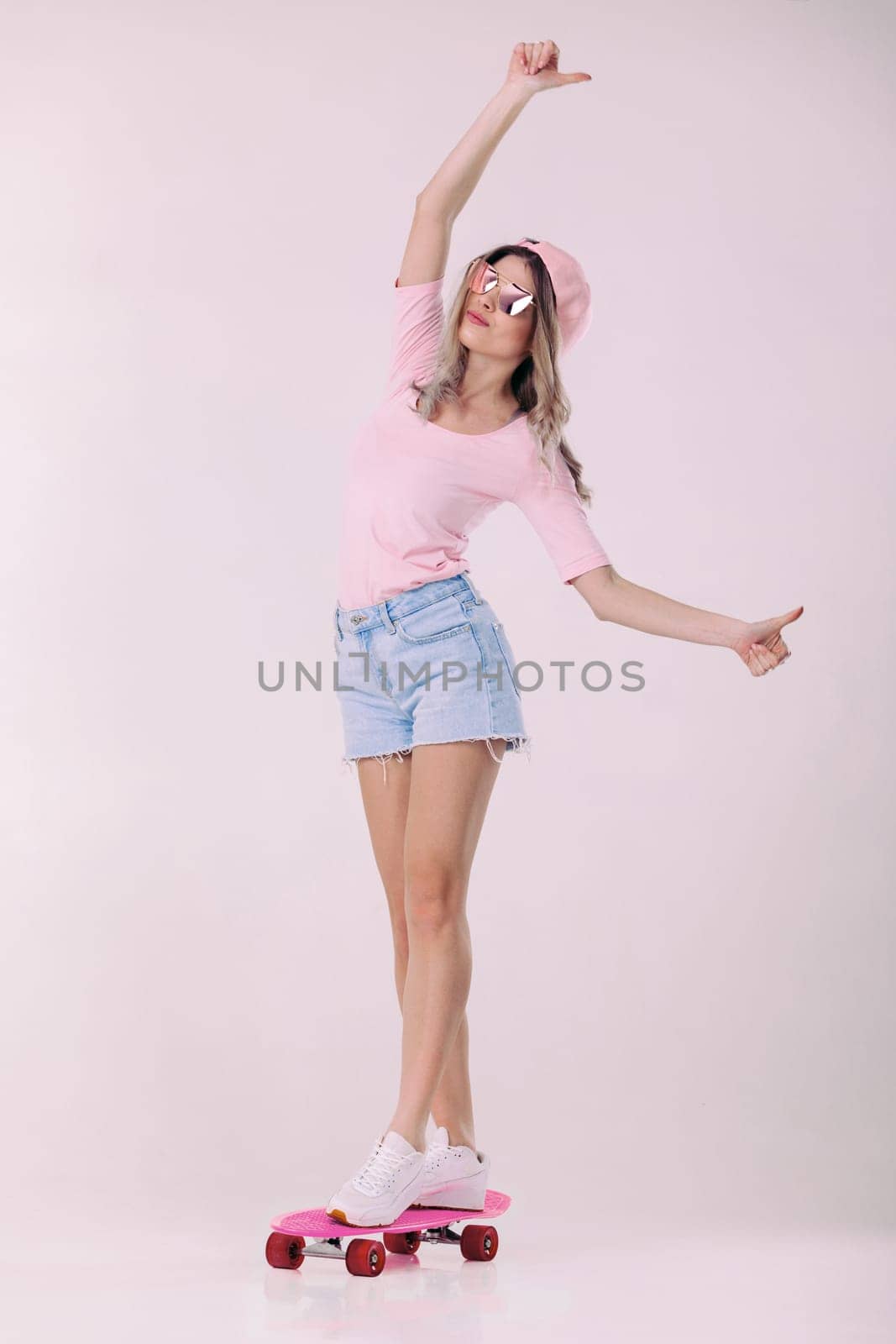 beautiful woman in sunglasses, pink t-shirt and cap stands on pink skateboard