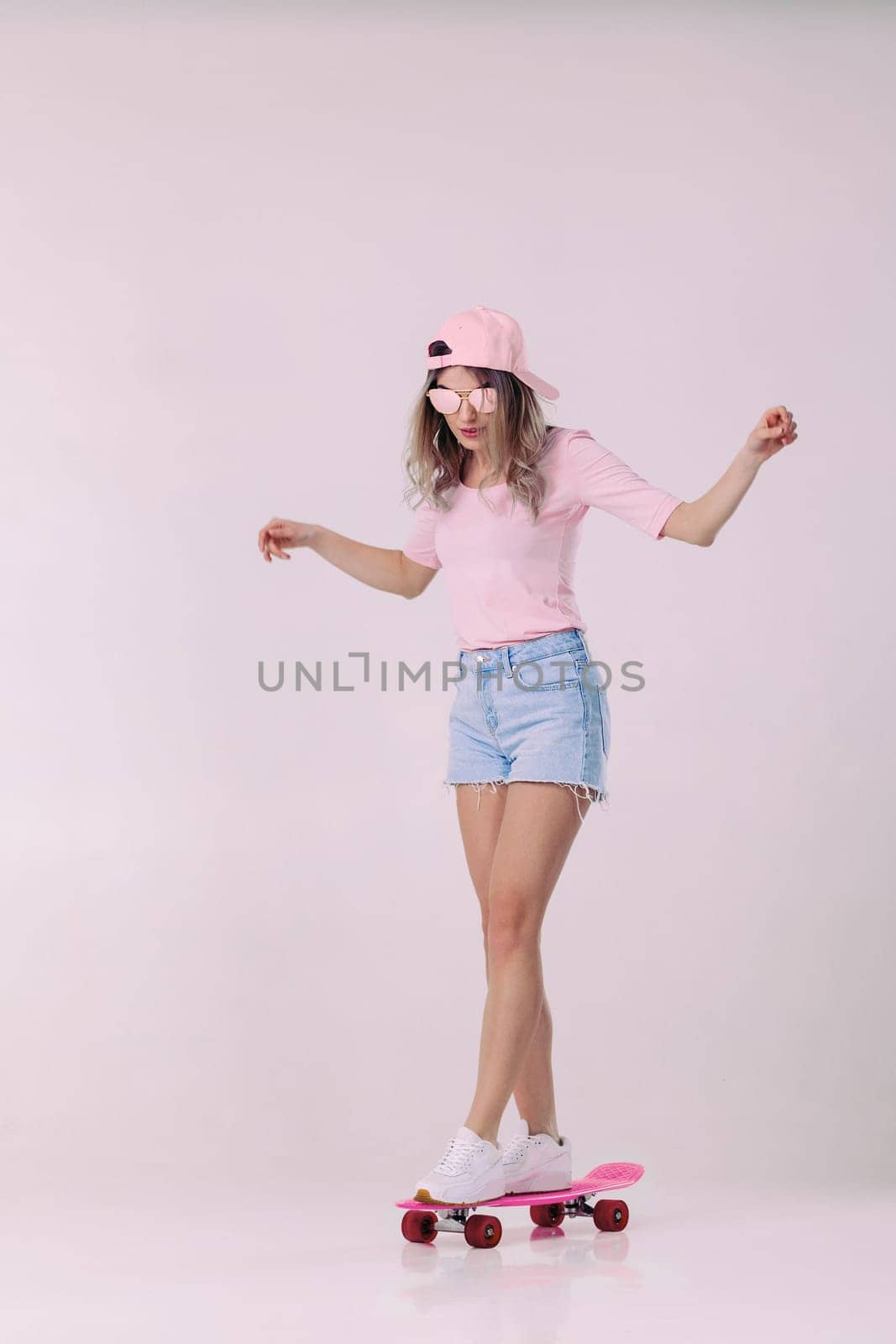 beautiful woman in sunglasses, pink t-shirt and cap stands on pink skateboard