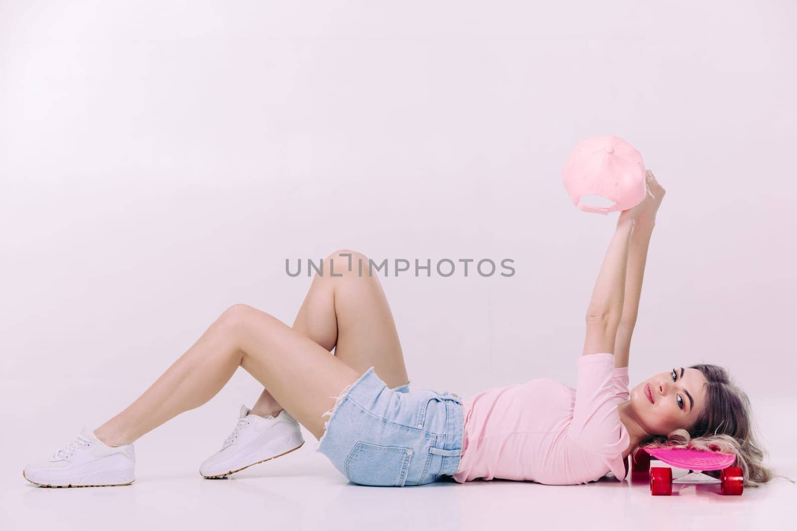 beautiful woman in pink t-shirt and cap lies on pink skateboard. relax and pleasure