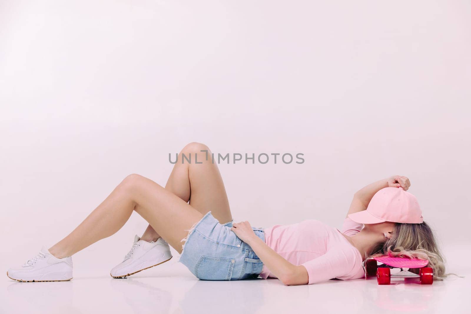 beautiful woman in pink t-shirt and cap lies on pink skateboard. relax and pleasure