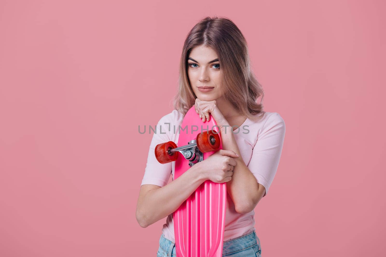 beautiful blonde woman in pink t-shirt and denim shorts hugs pink skateboard