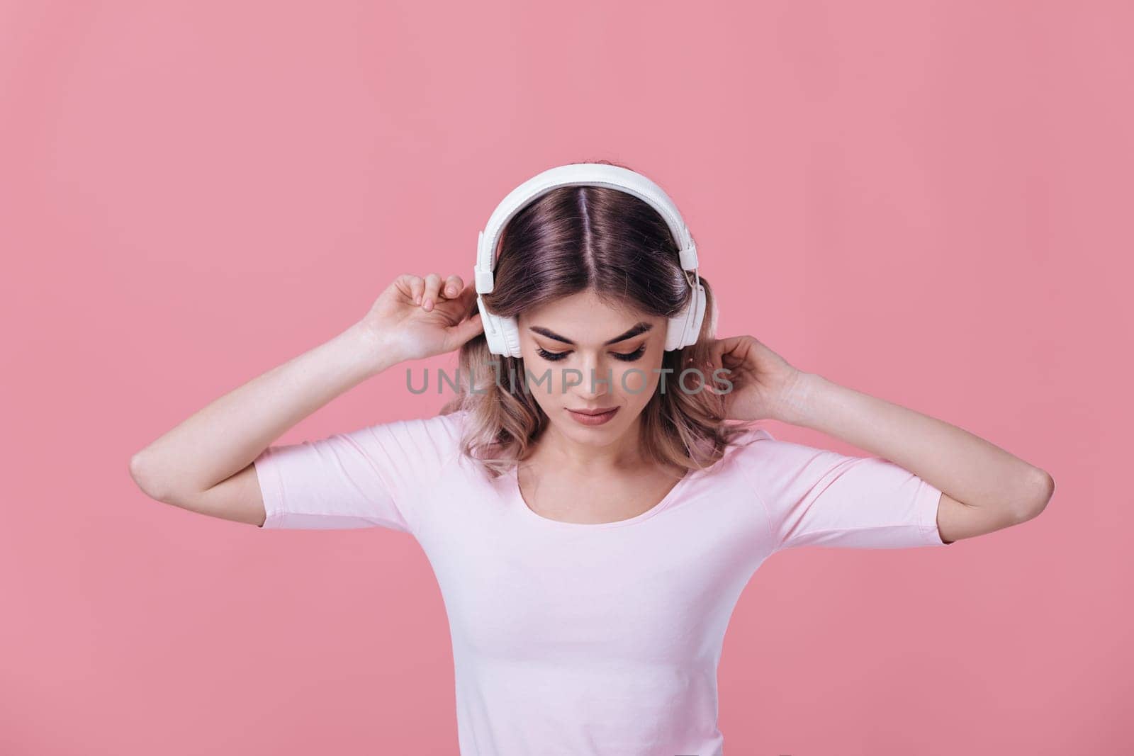 beautiful blonde woman in pink t-shirt and white headphones enjoying listens to music on pink background