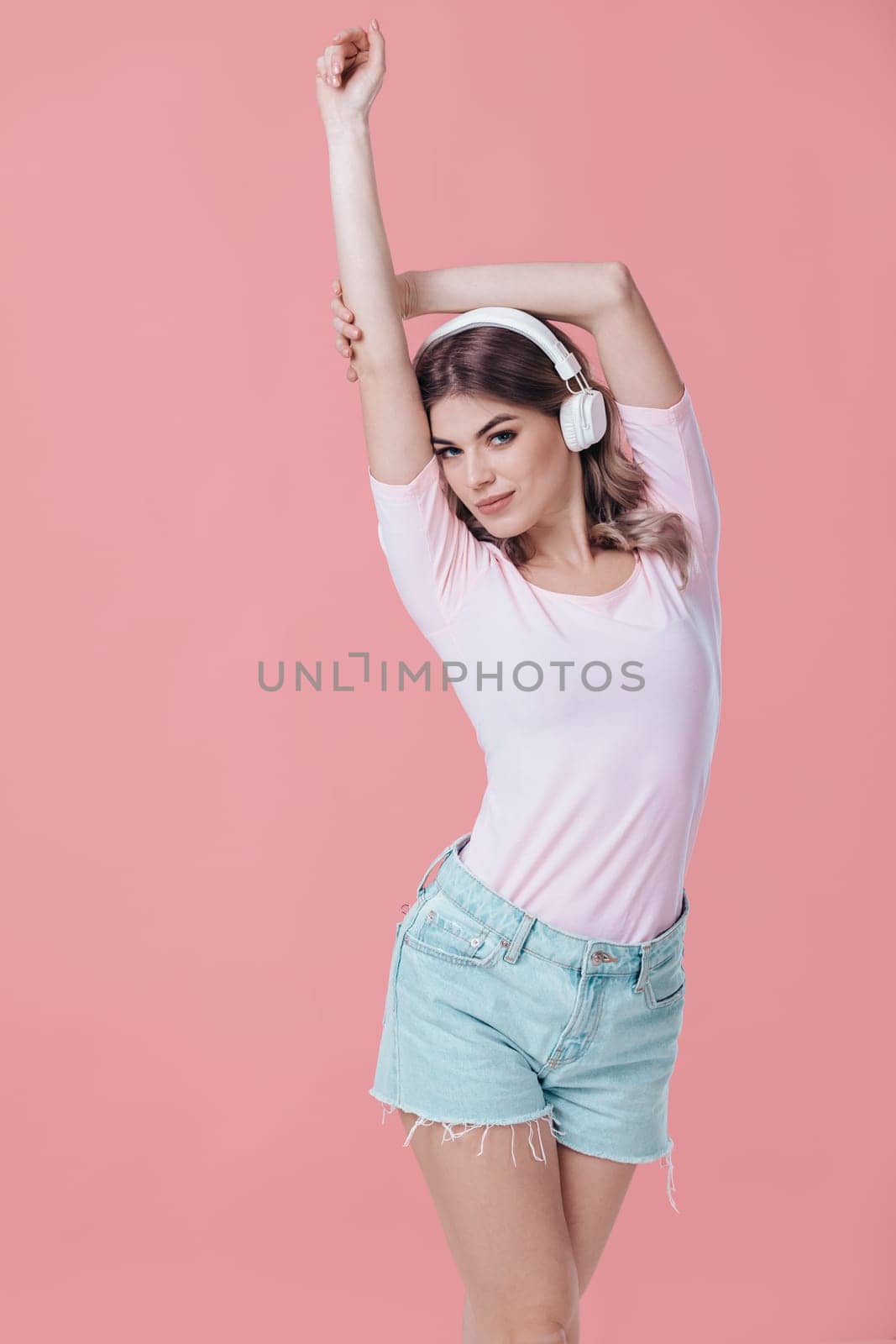 beautiful blonde woman in pink t-shirt and white headphones enjoying listens to music on pink background