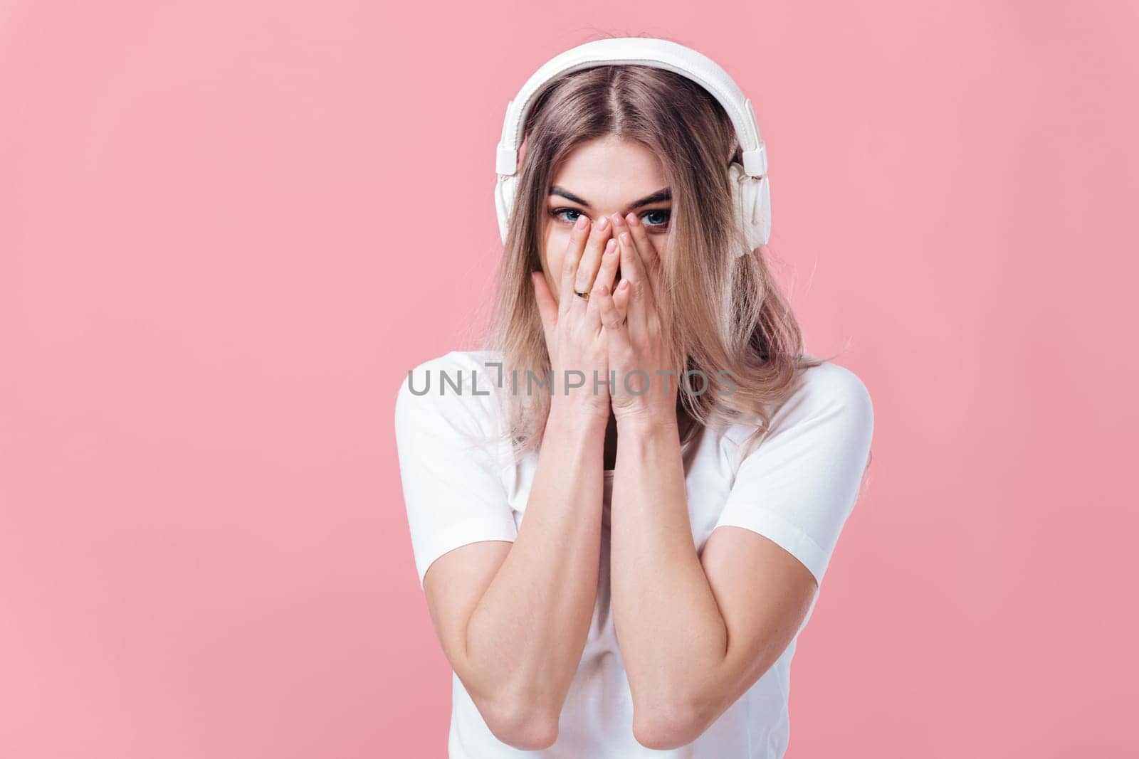 beautiful blonde woman in t-shirt and white headphones listens to music on pink background