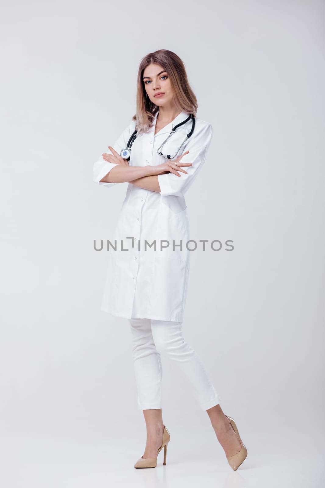 Medical physician doctor woman in white coat with stethoscope looks at camera on light background.