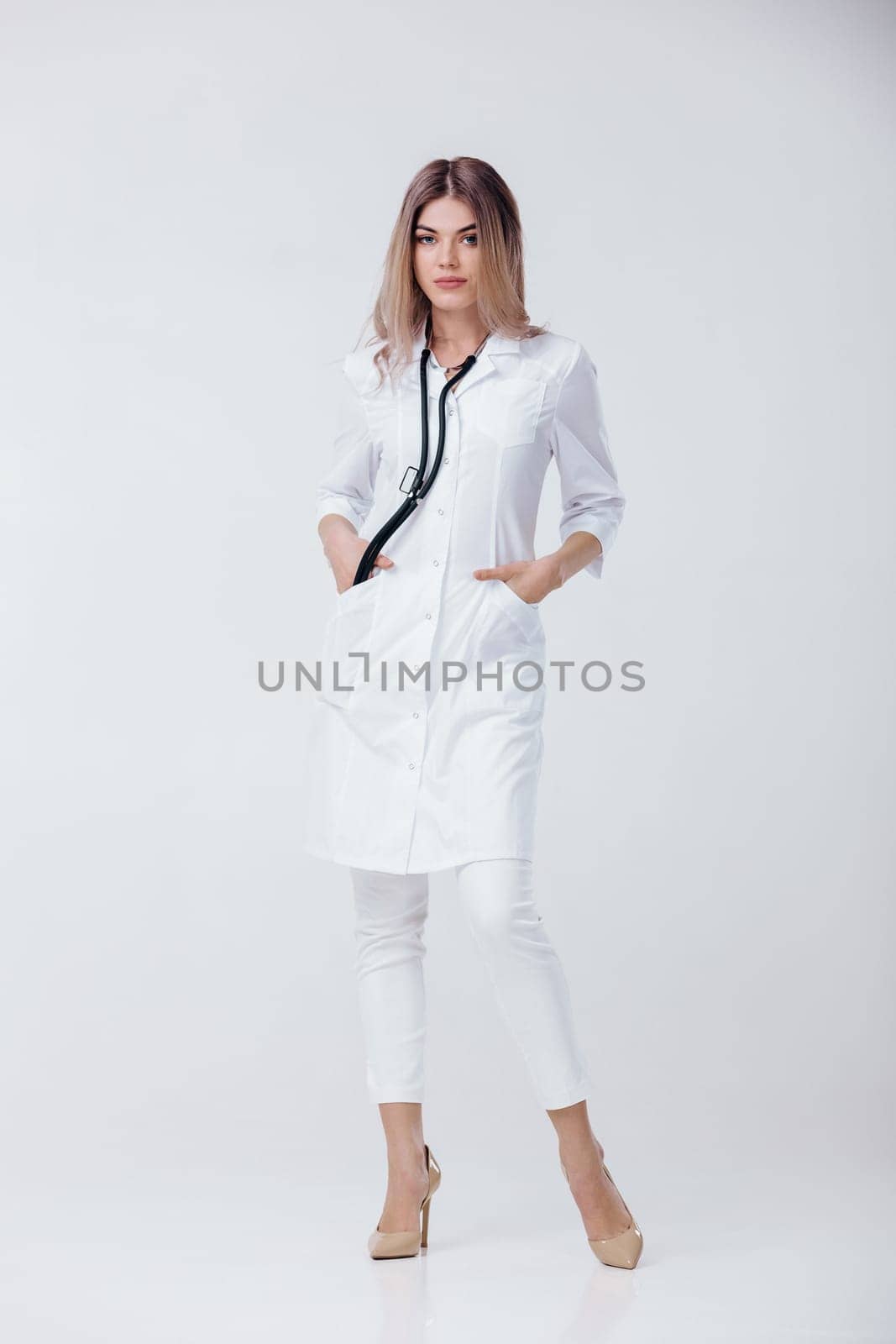 Full length portrait of medical physician doctor woman in white coat with stethoscope on light background.