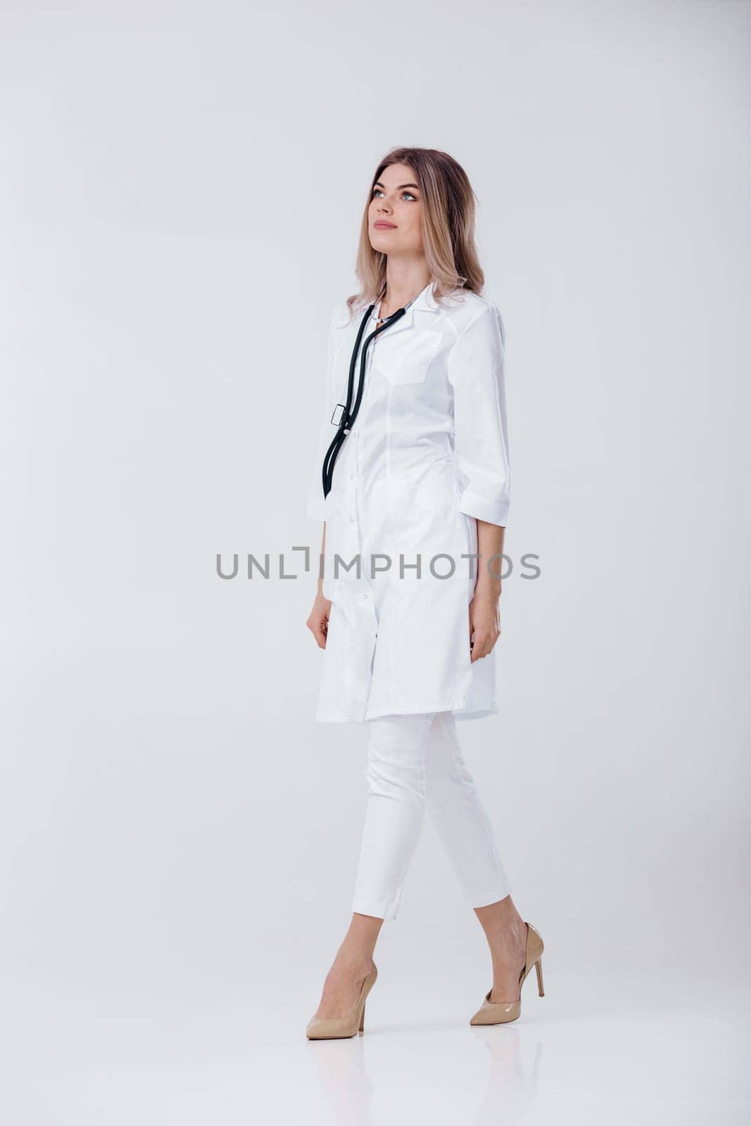 Full length portrait of medical physician doctor woman in white coat with stethoscope on light background.