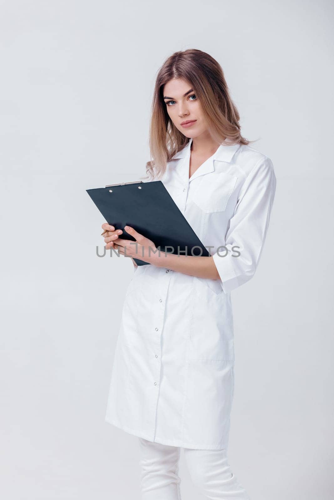 Medical physician doctor woman in white coat holds folder with documents and looks at camera on light background.