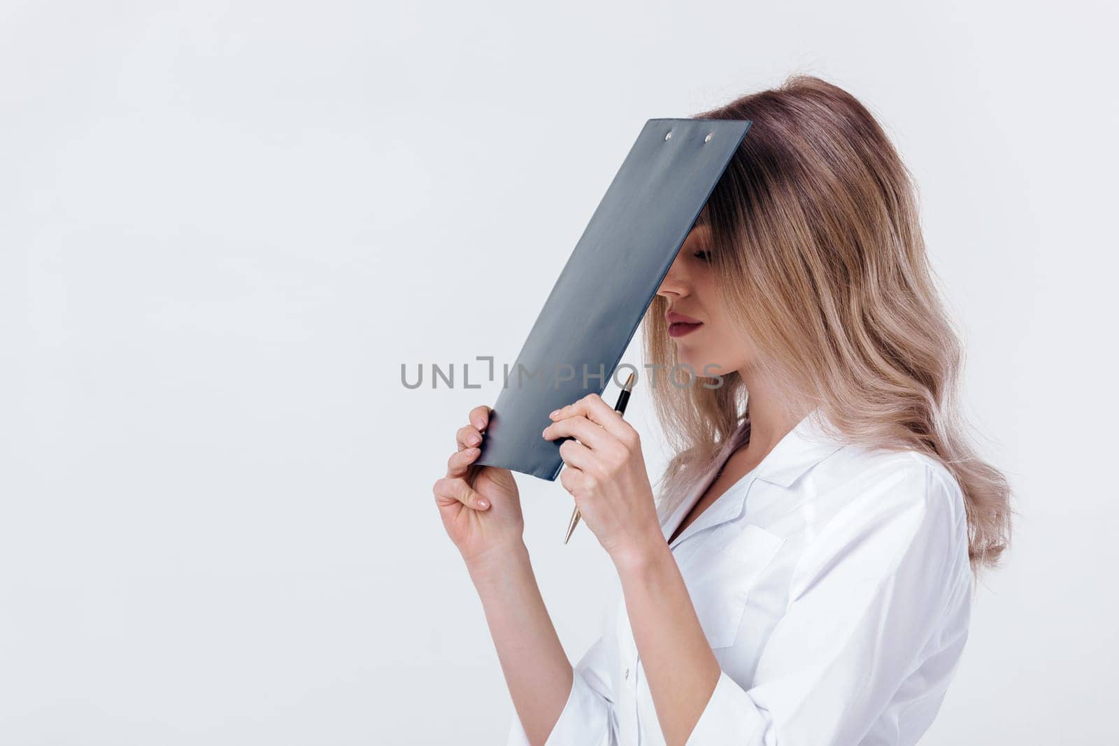 tired medical physician doctor woman in white coat holds folder with documents on light background.