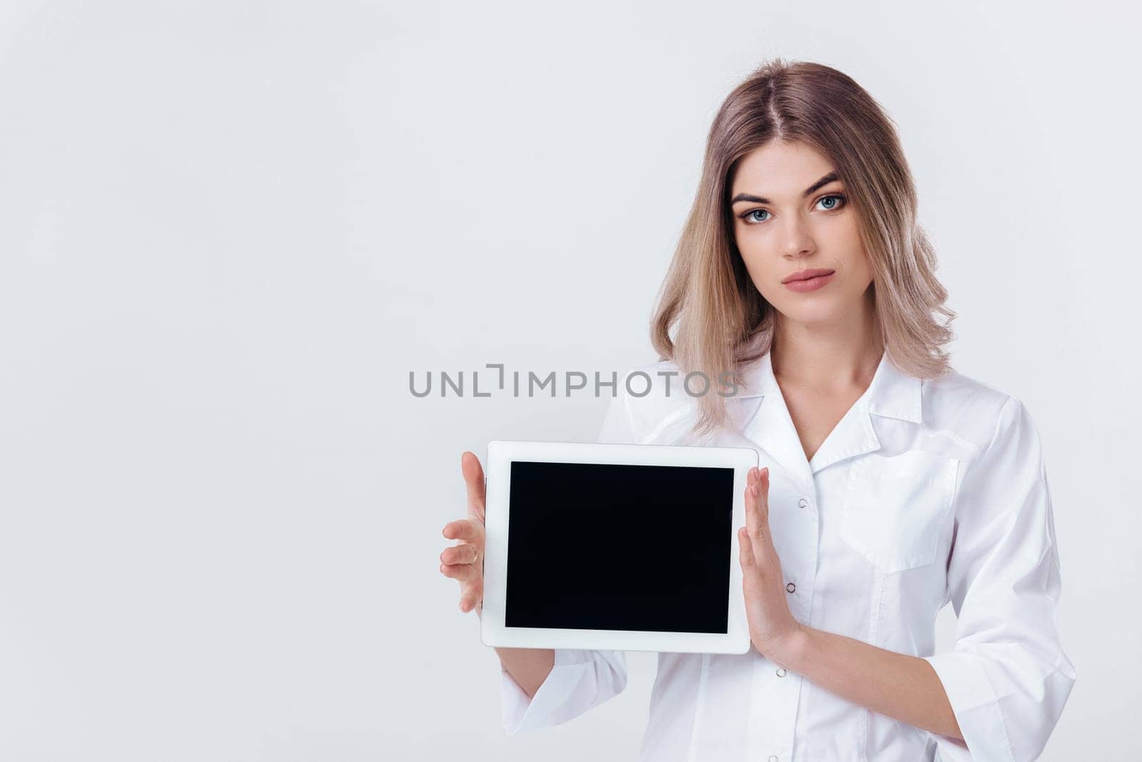 Portrait of beautiful blonde doctor in white coat showing screen of digital tablet in her hand. Healthcare and technology concept.