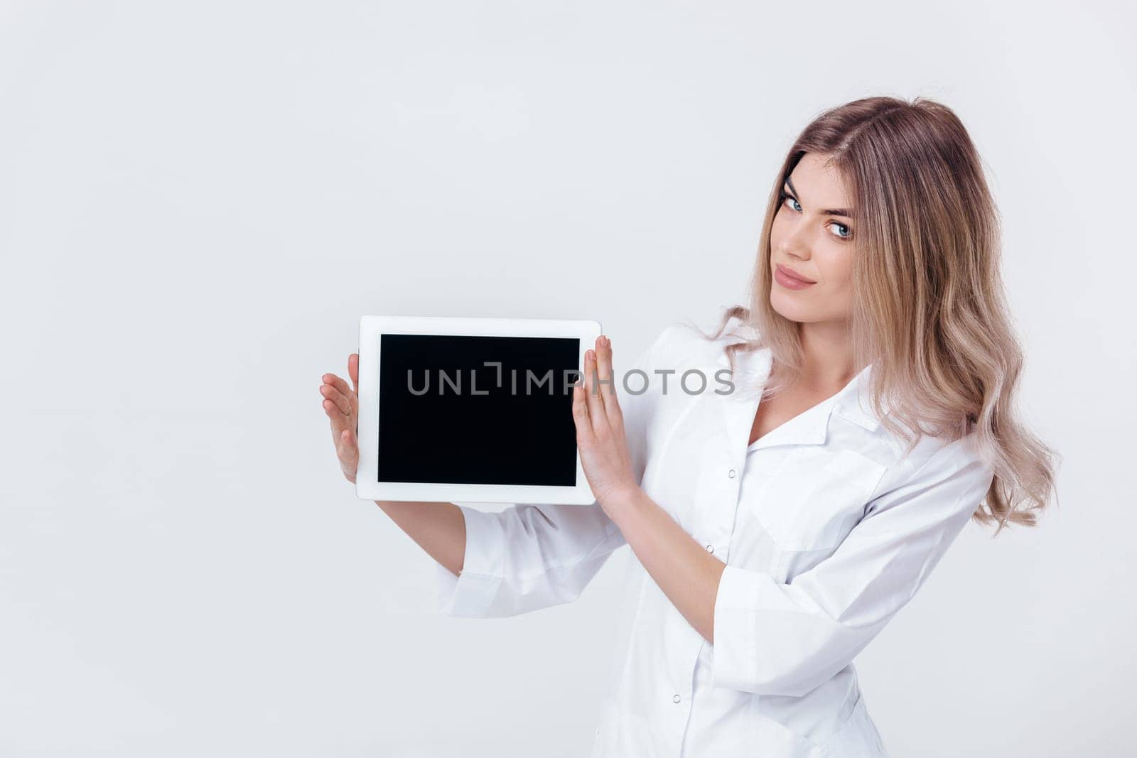Portrait of smiling blonde doctor in white coat showing screen of digital tablet in her hand. Healthcare and technology concept.