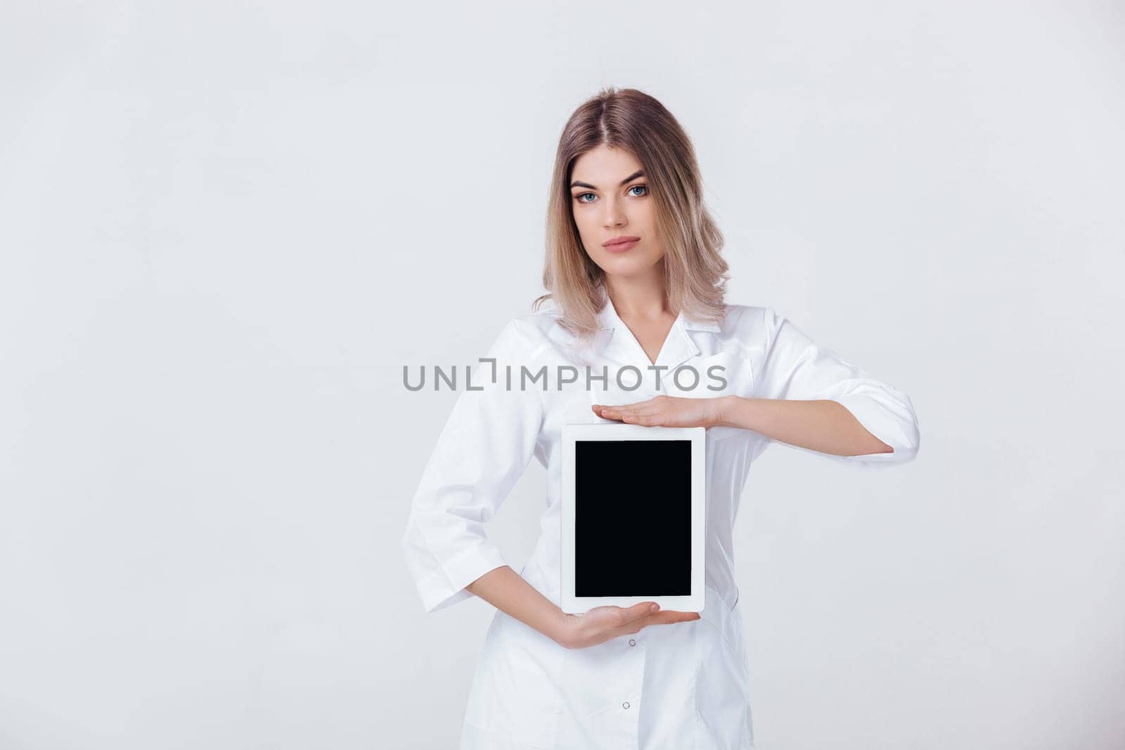 Portrait of beautiful blonde doctor in white coat showing screen of digital tablet in her hand. Healthcare and technology concept.
