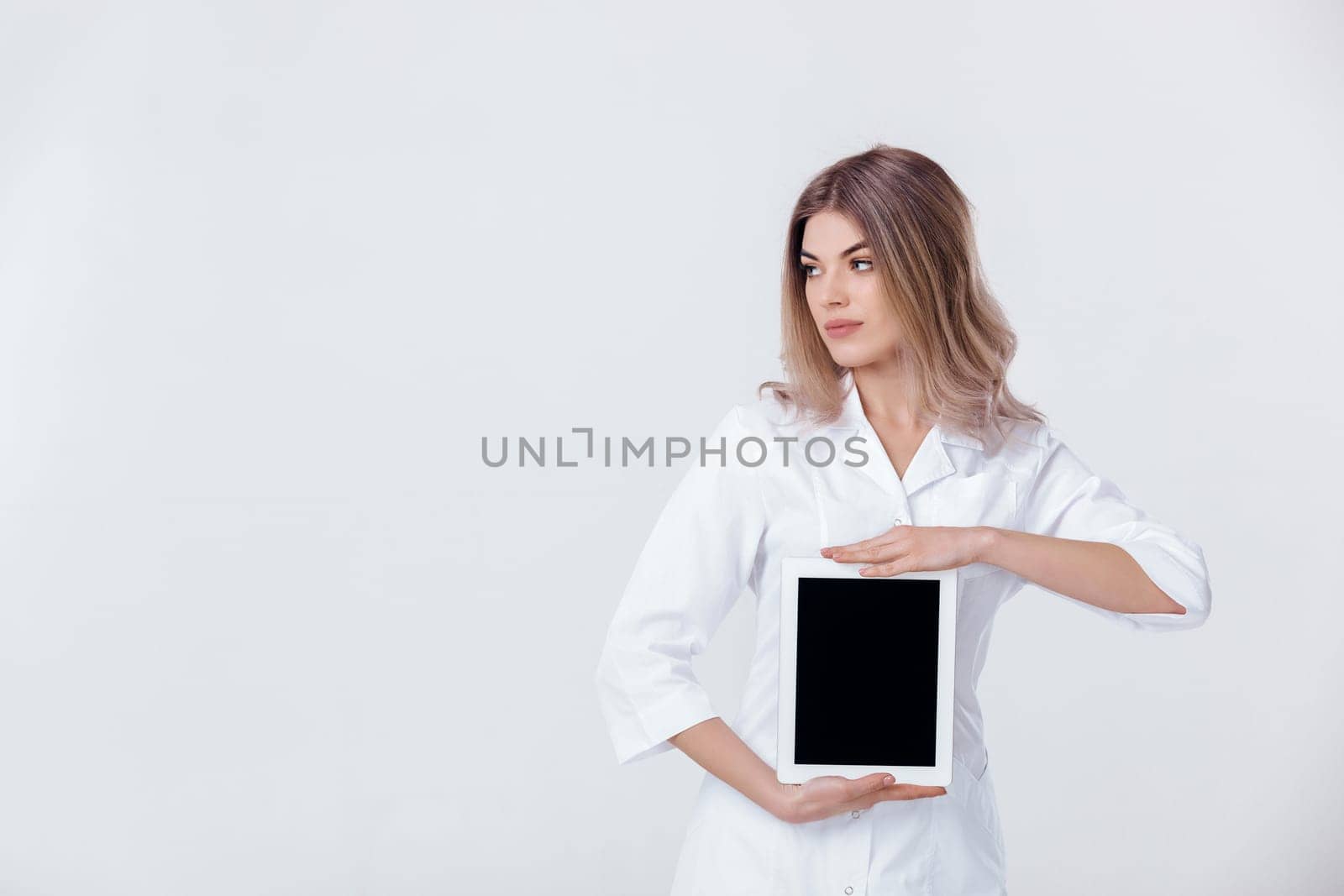 Portrait of beautiful blonde doctor in white coat showing screen of digital tablet in her hand. Healthcare and technology concept.