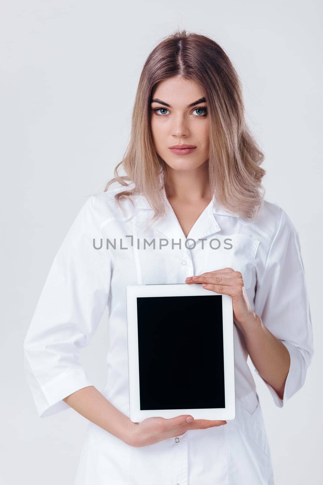 Portrait of beautiful blonde doctor in white coat showing screen of digital tablet in her hand. Healthcare and technology concept.