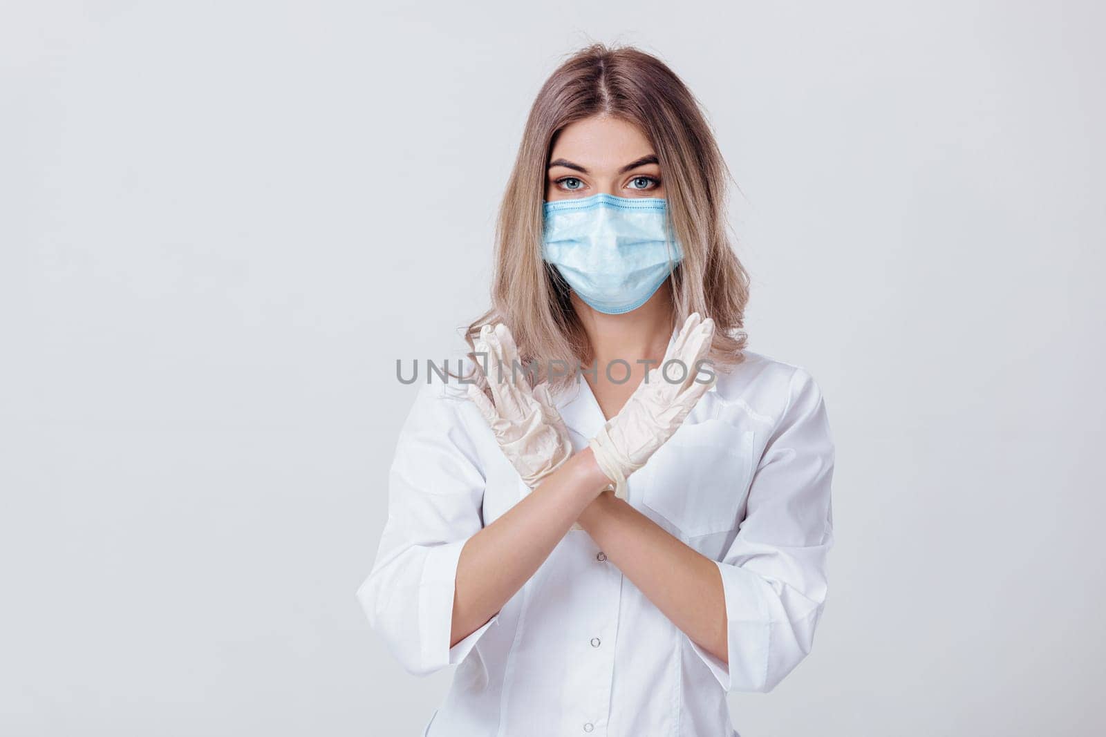Portrait of woman doctor with face mask and white medical gloves shows stop sign