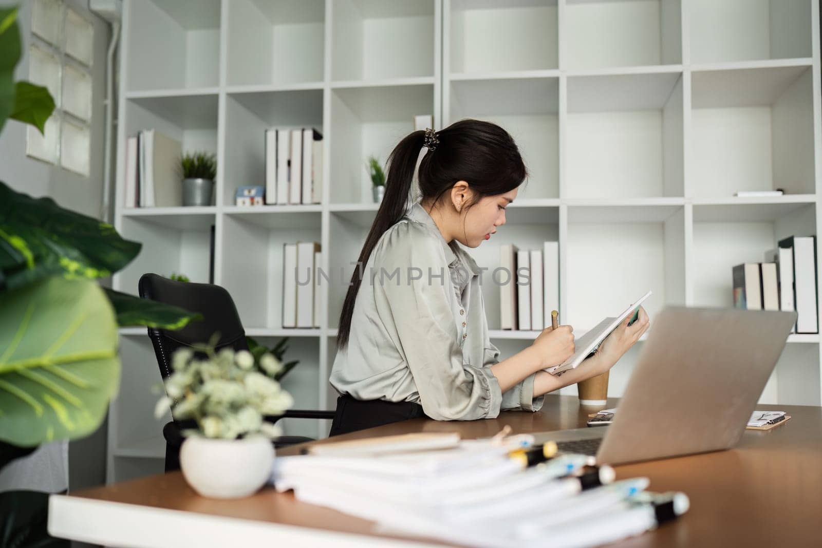 business woman working with laptop while consulting some invoice and document in working space at home by itchaznong